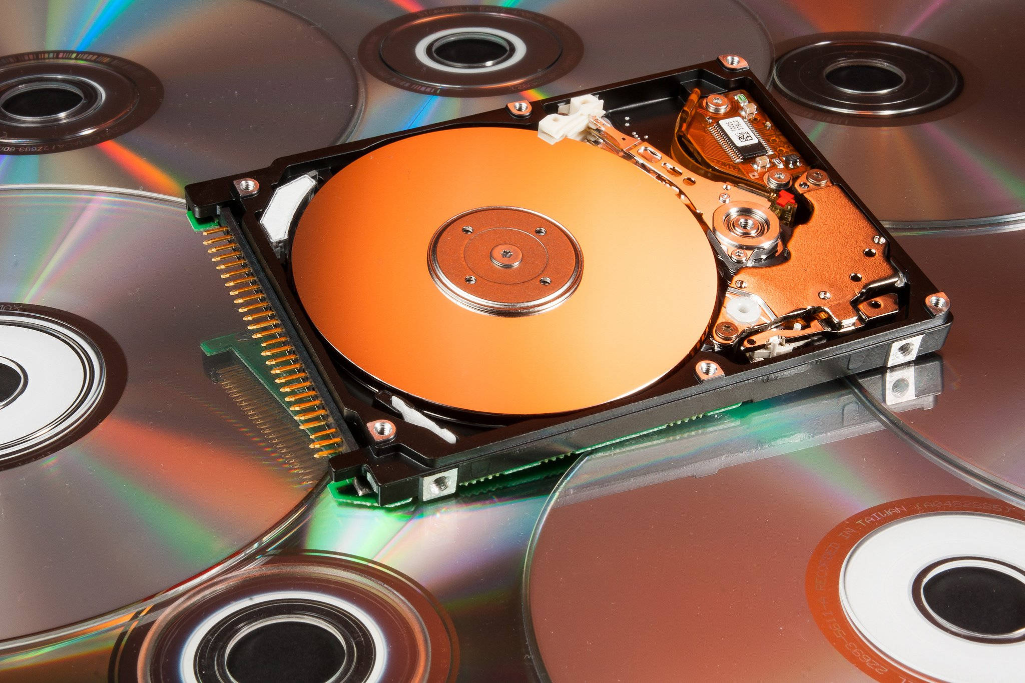 Hard Drive 桌布 壁紙 — 一個拆解的硬碟，帶有橙色碟片，放置在反光的CD和DVD之上。
