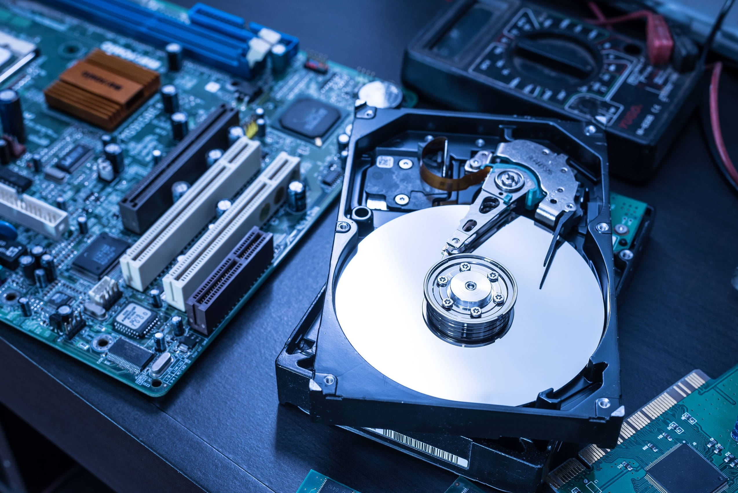 Processor 桌布 壁紙 — 一個拆解的硬碟放在主機板上，附近有工具，在冷藍色燈光下。