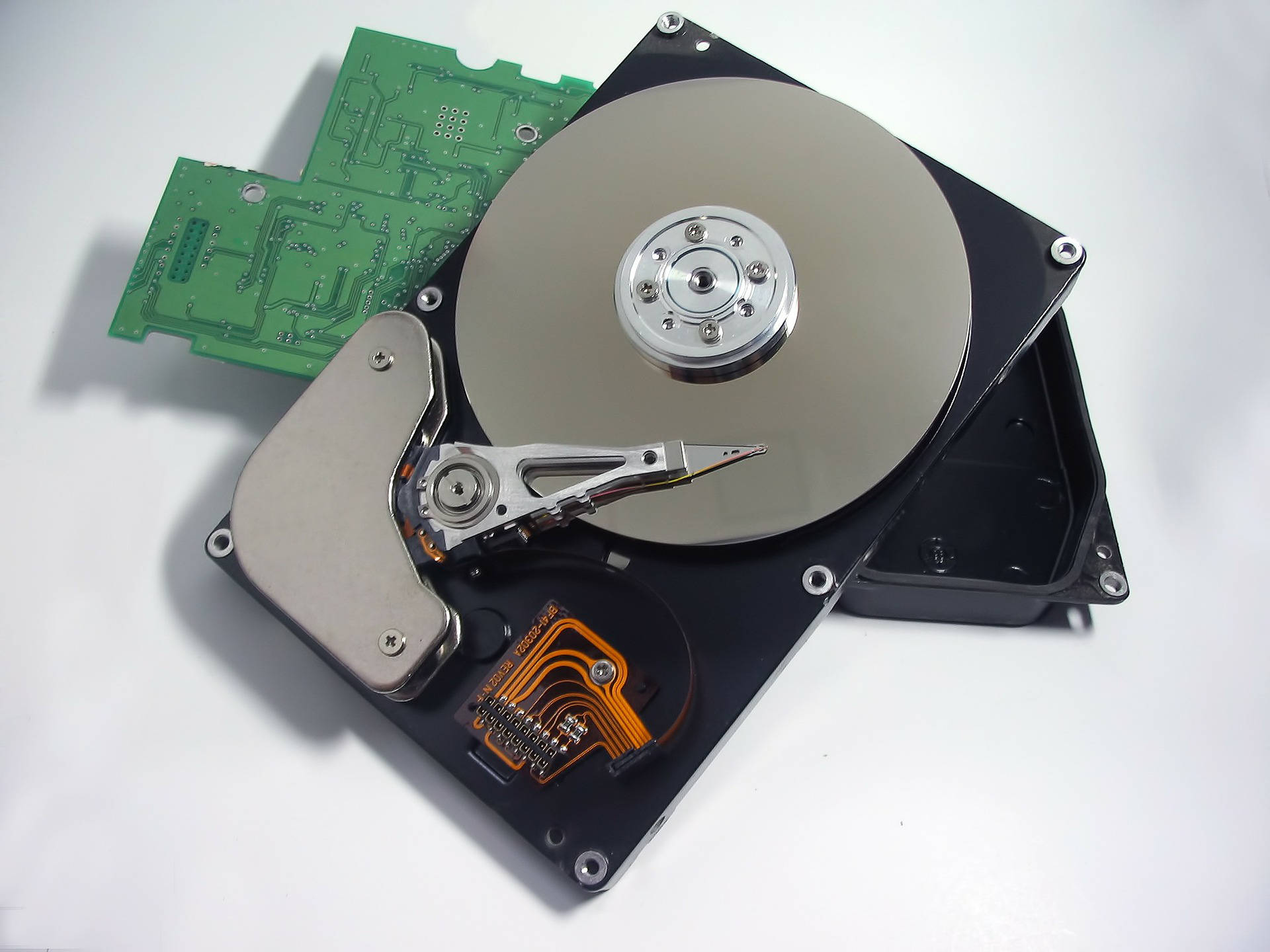 Hard Drive 桌布 壁紙 — 一個拆解的硬碟機，暴露的碟片、電路板和讀寫臂放在乾淨的白色表面上。