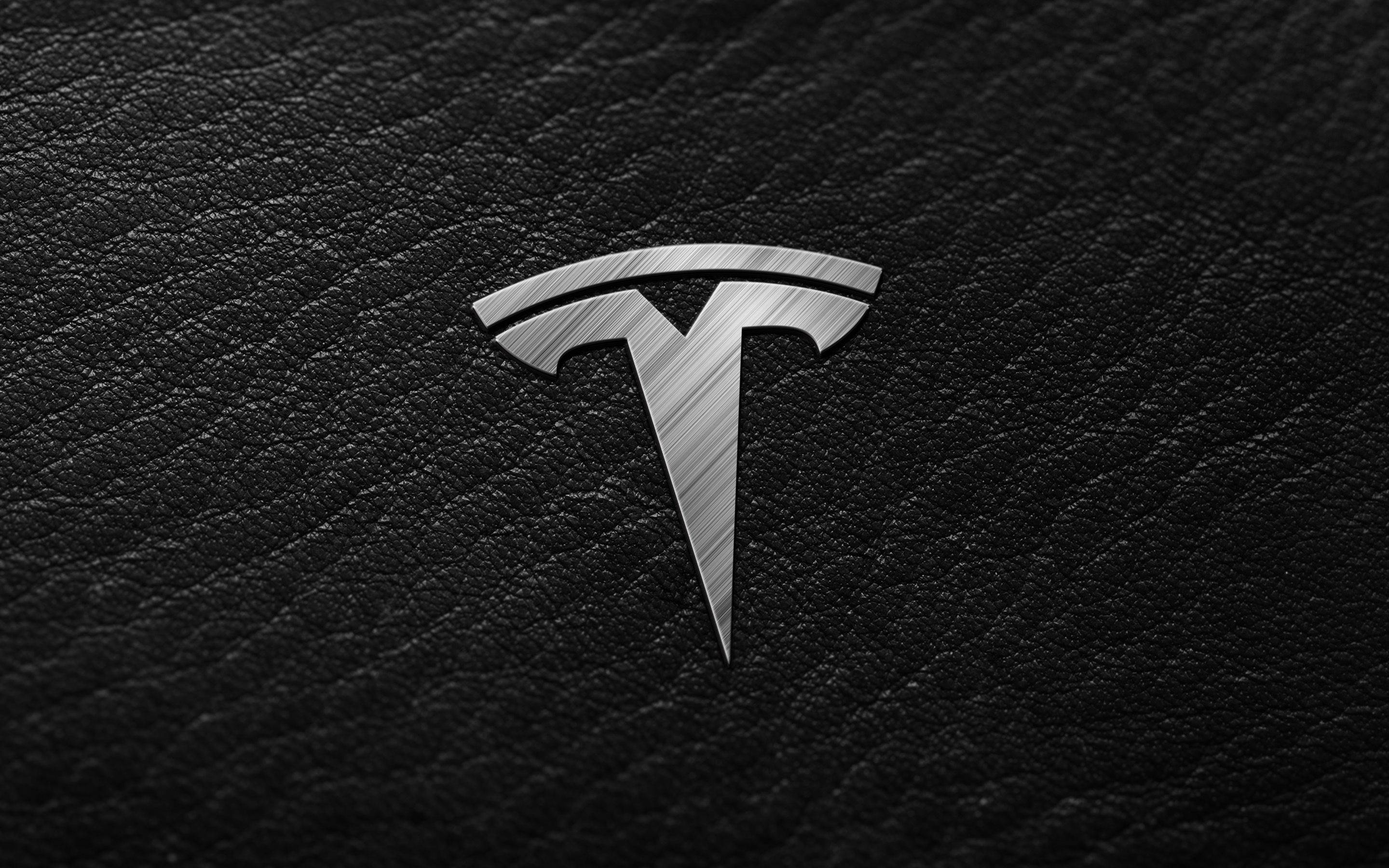 特斯拉 桌布 壁紙 — 一個拉絲金屬 Tesla 標誌在帶有紋理的黑色皮革背景上閃耀。