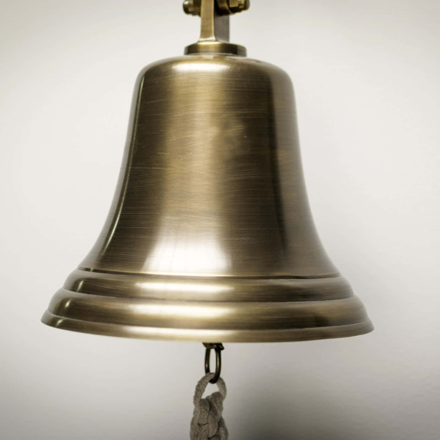 Bell 桌布 壁紙 — 一個拉絲黃銅鈴鐺的特寫，帶有繩索拉環，懸掛在純白色背景上。