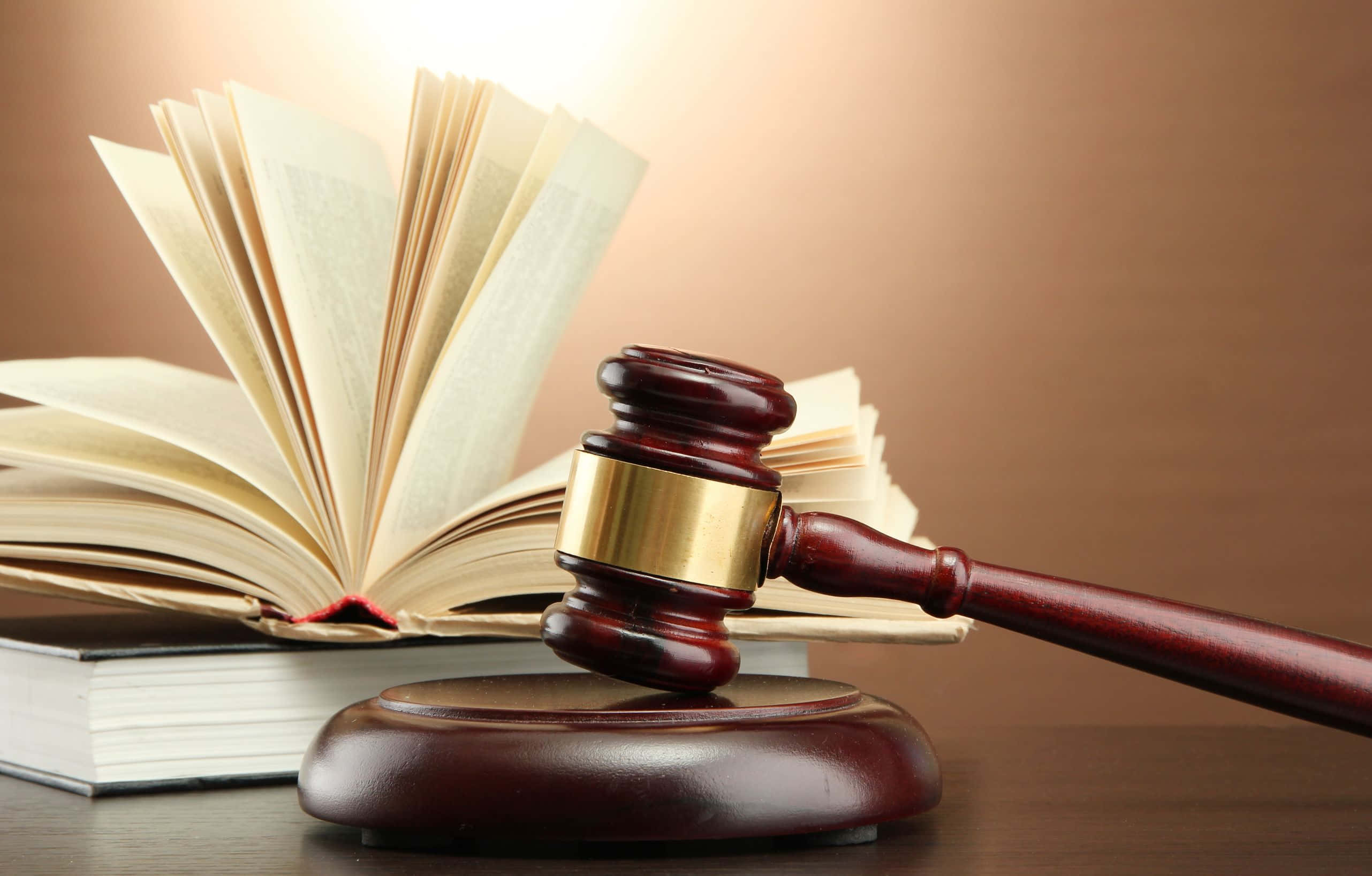 Law 桌布 壁紙 — 一個拋光木槌放在其支架上，旁邊有一本打開的書，書頁在溫暖的背光下展開。