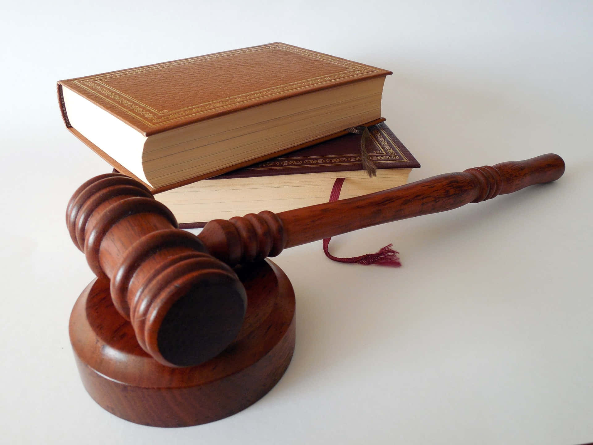 Law 桌布 壁紙 — 一個拋光木槌放在其支架上，旁邊有兩本皮革裝訂的法律書籍，置於純白表面上。