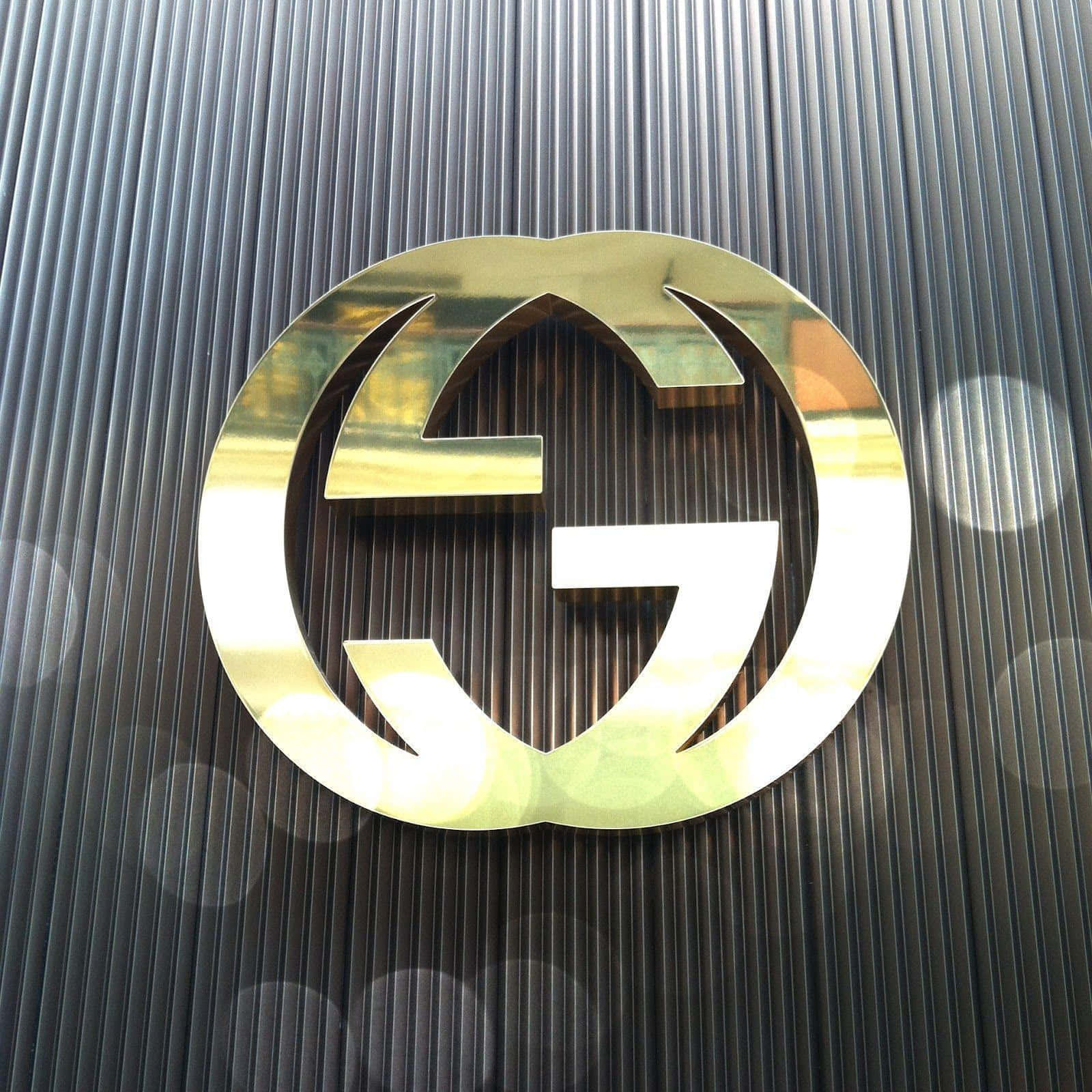 Gucci 桌布 壁紙 — 一個拋光金色Gucci標誌徽章在帶有柔和散景高光的深色垂直條紋牆上閃耀。