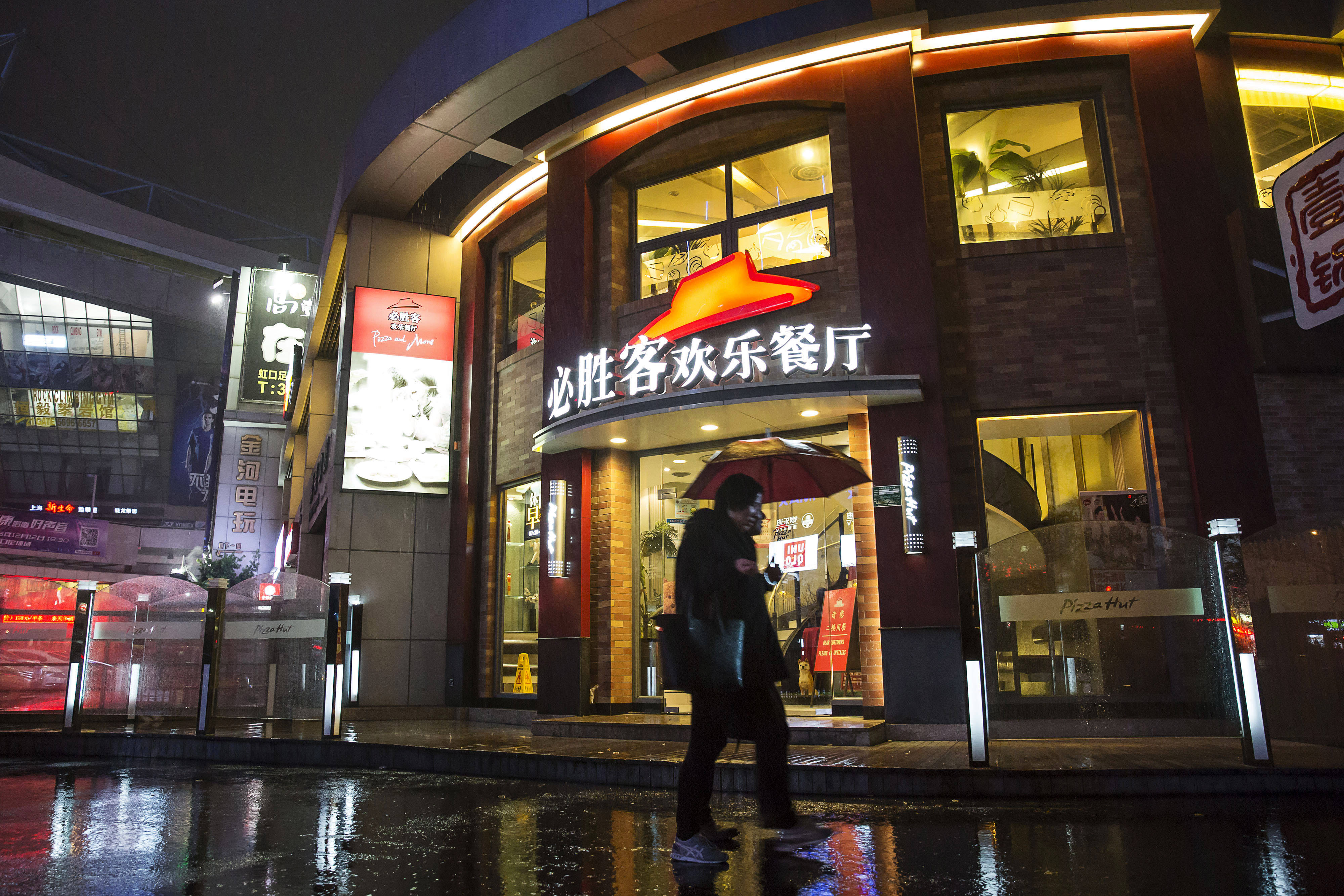 Hut 桌布 壁紙 — 一個拿著雨傘的人夜晚在濕漉漉的、反射著霓虹燈光的城市街道上走過燈火通明的必勝客。