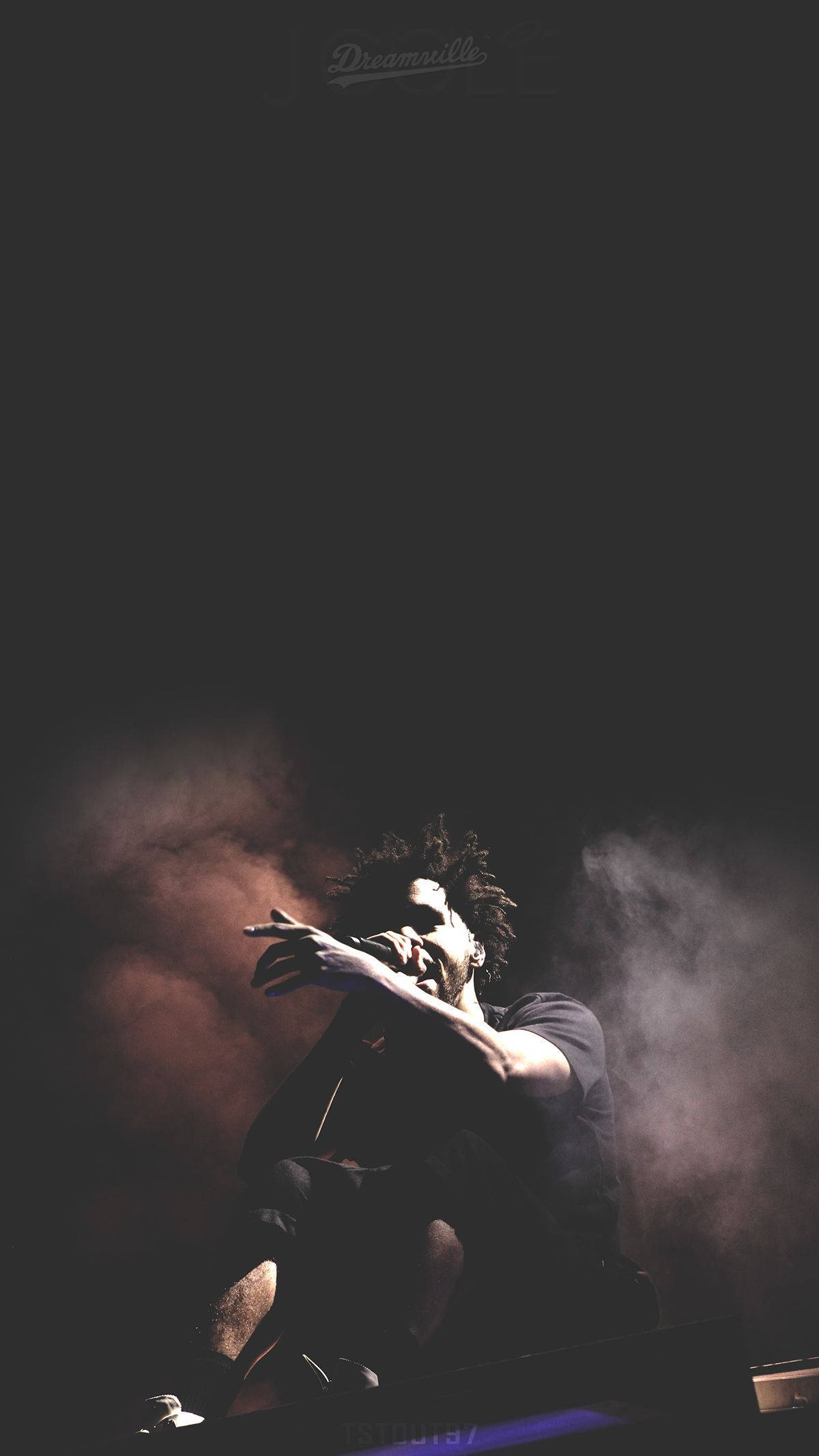 J Cole 桌布 壁紙 — 一個捲髮剪影表演者在戲劇性的舞台燈光和煙霧中對著麥克風唱歌。