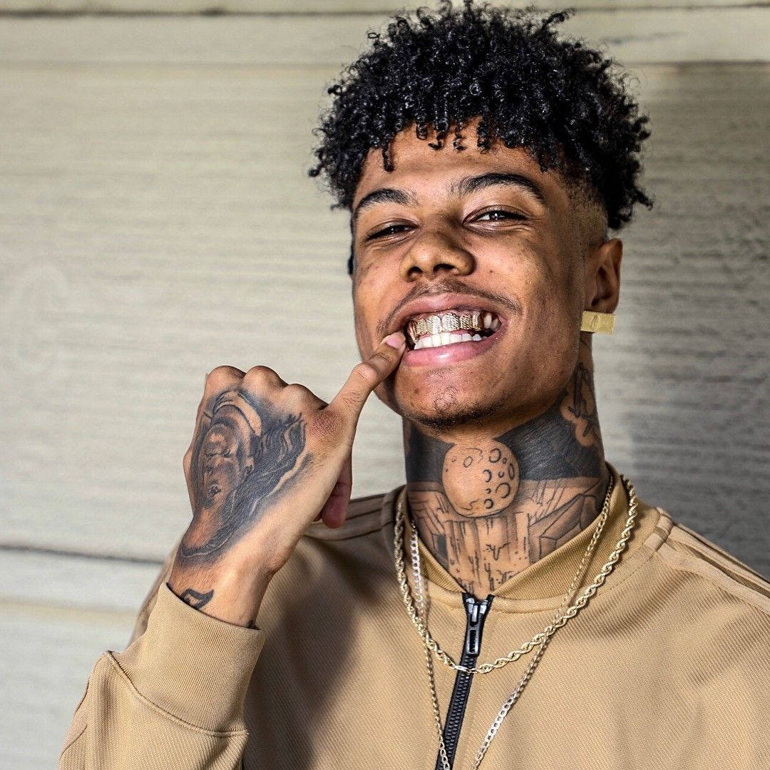 Celebrity 桌布 壁紙 — 一個捲髮及刺青的年輕男子微笑著指向他的鑽石牙套，背景是木牆。