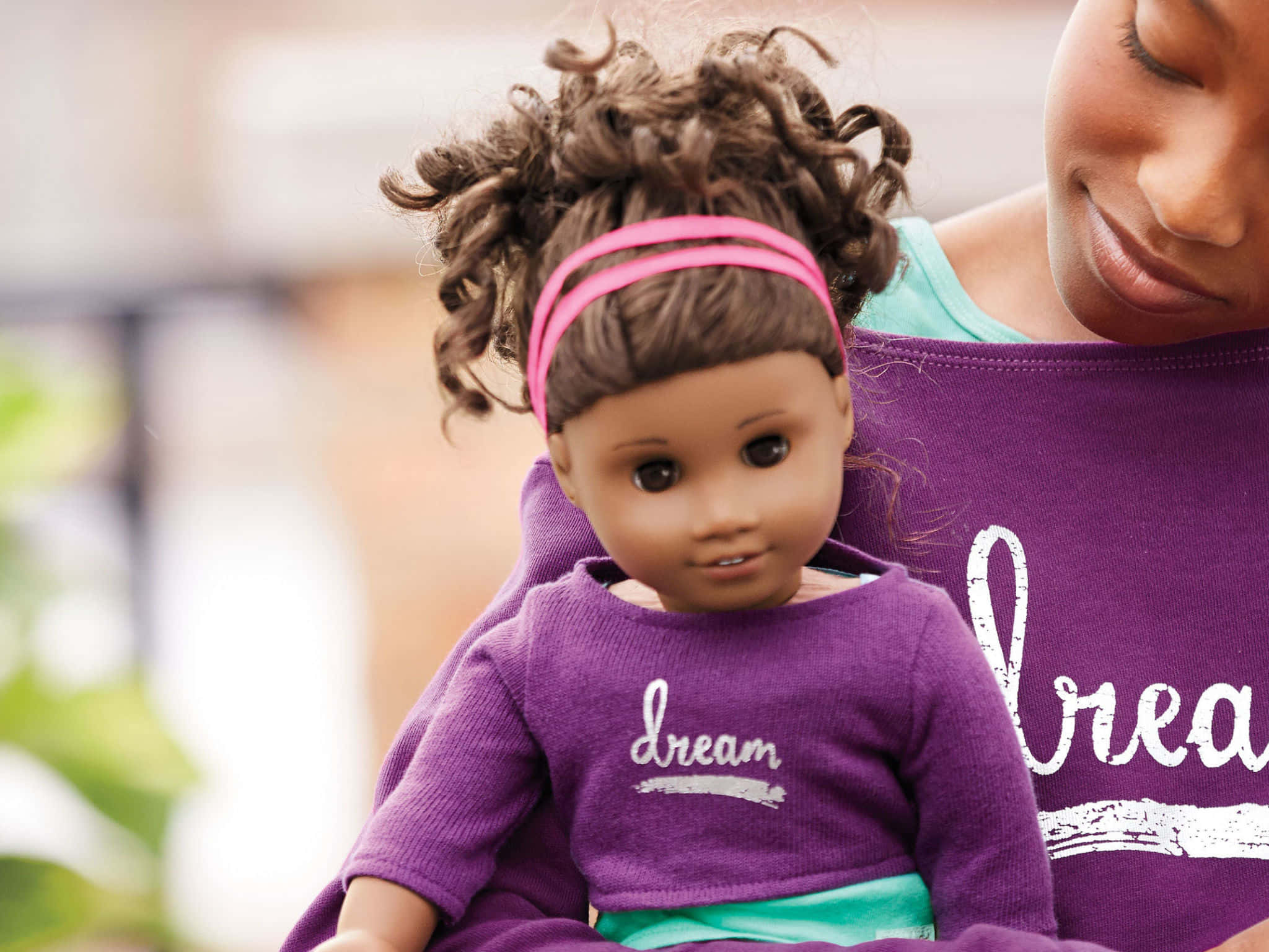 american girl 桌布 壁紙 — 一個捲髮女孩戴著粉紅色頭帶，抱著一個穿著紫色衣服的洋娃娃，上面印有「夢想」這個詞。