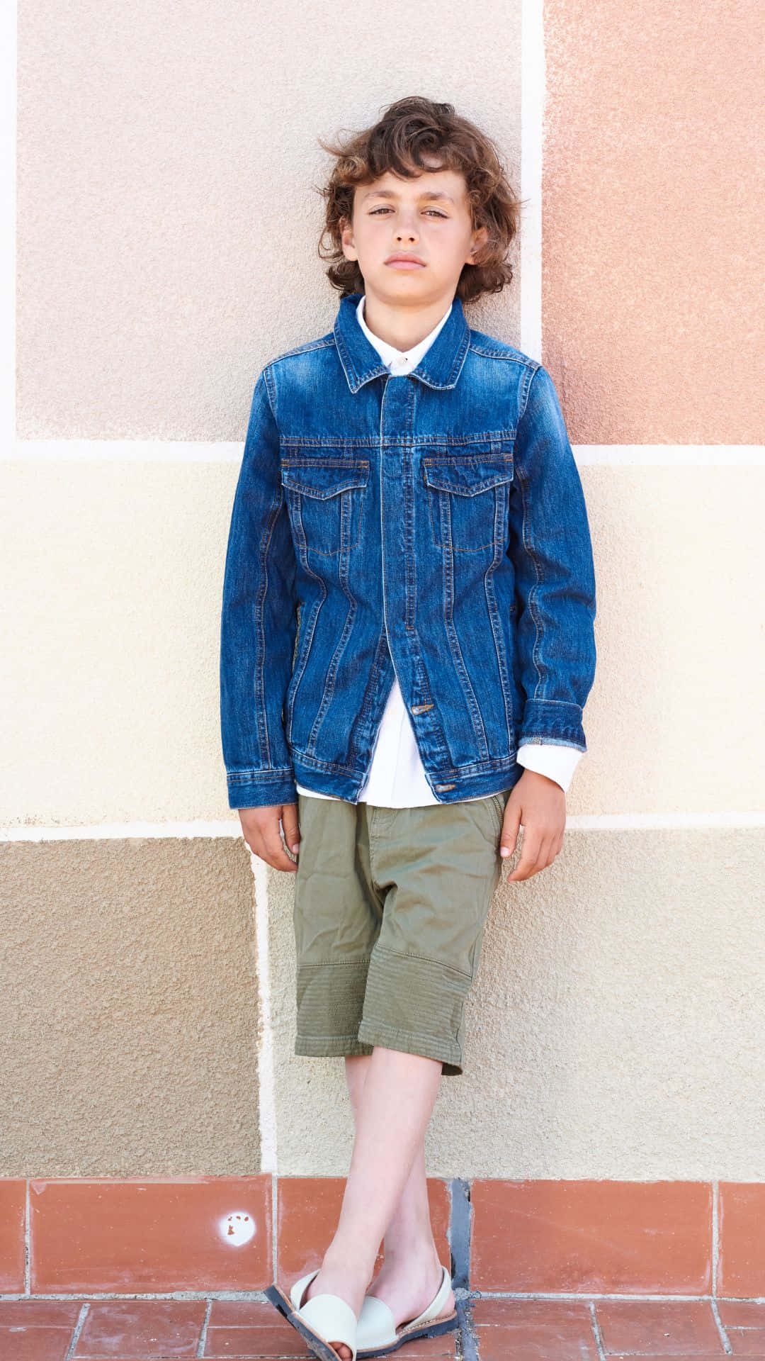Denim 桌布 壁紙 — 一個捲髮小男孩自信地站在粉彩色牆前，身穿牛仔外套和卡其色短褲。
