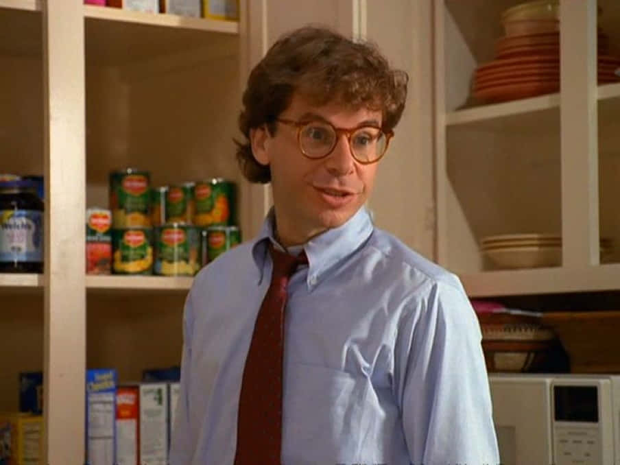 rick moranis 桌布 壁紙 — 一個捲髮戴眼鏡的男人站在廚房儲藏室裡，周圍是罐頭食品和疊放的盤子。