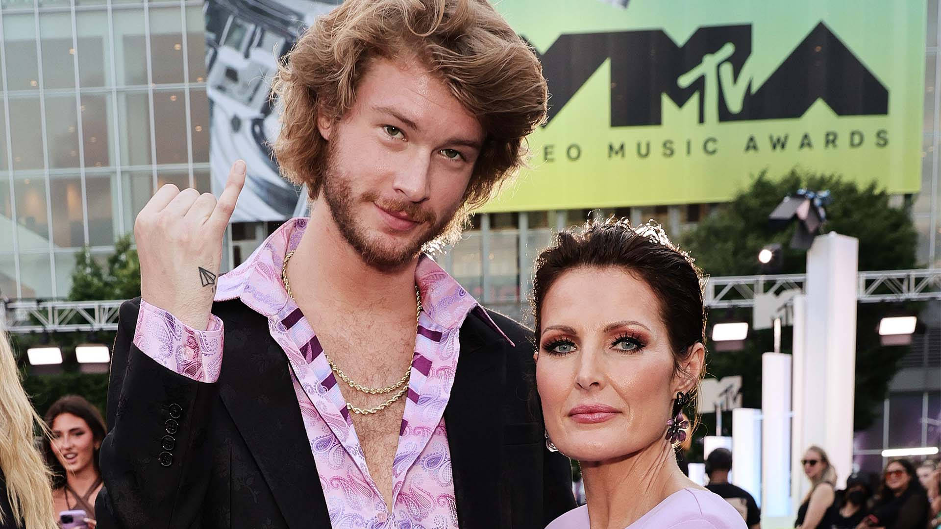 情侶 桌布 壁紙 — 一個捲髮男人和一個女人在MTV Video Music Awards的紅地毯上自信地擺姿勢，背景有明亮的燈光和綠色背景。