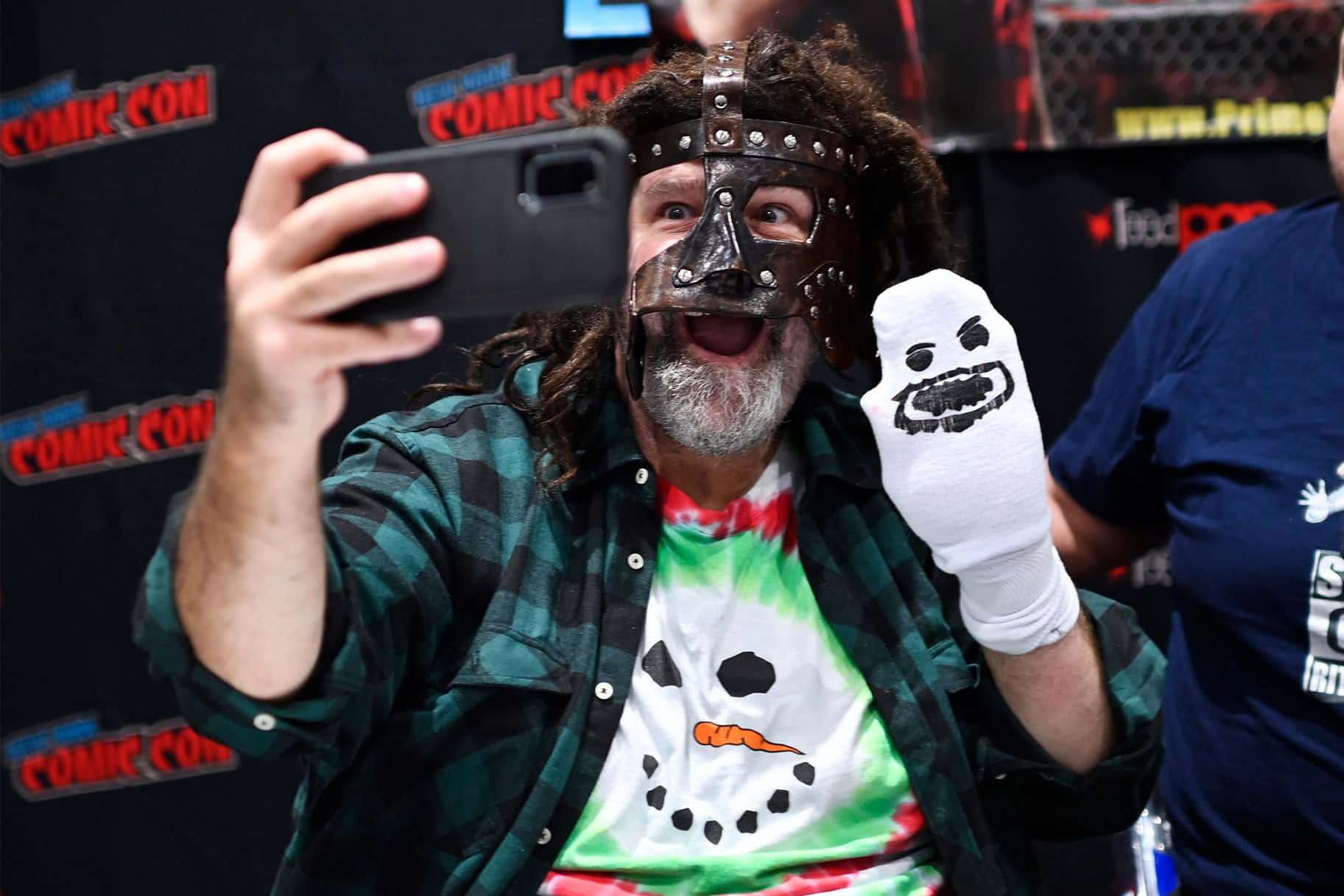 WWE 桌布 壁紙 — 一個捲髮男子戴著皮革面具和雪人襯衫，在動漫展活動中自拍。