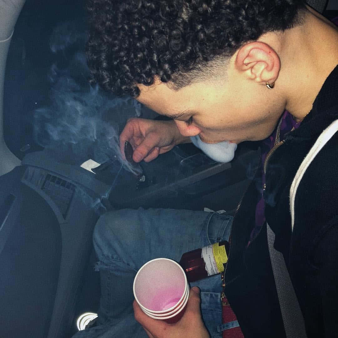 Lil Mosey 桌布 壁紙 — 一個捲髮的人在夜間在車內吸煙，手持粉紅色杯子和瓶子。