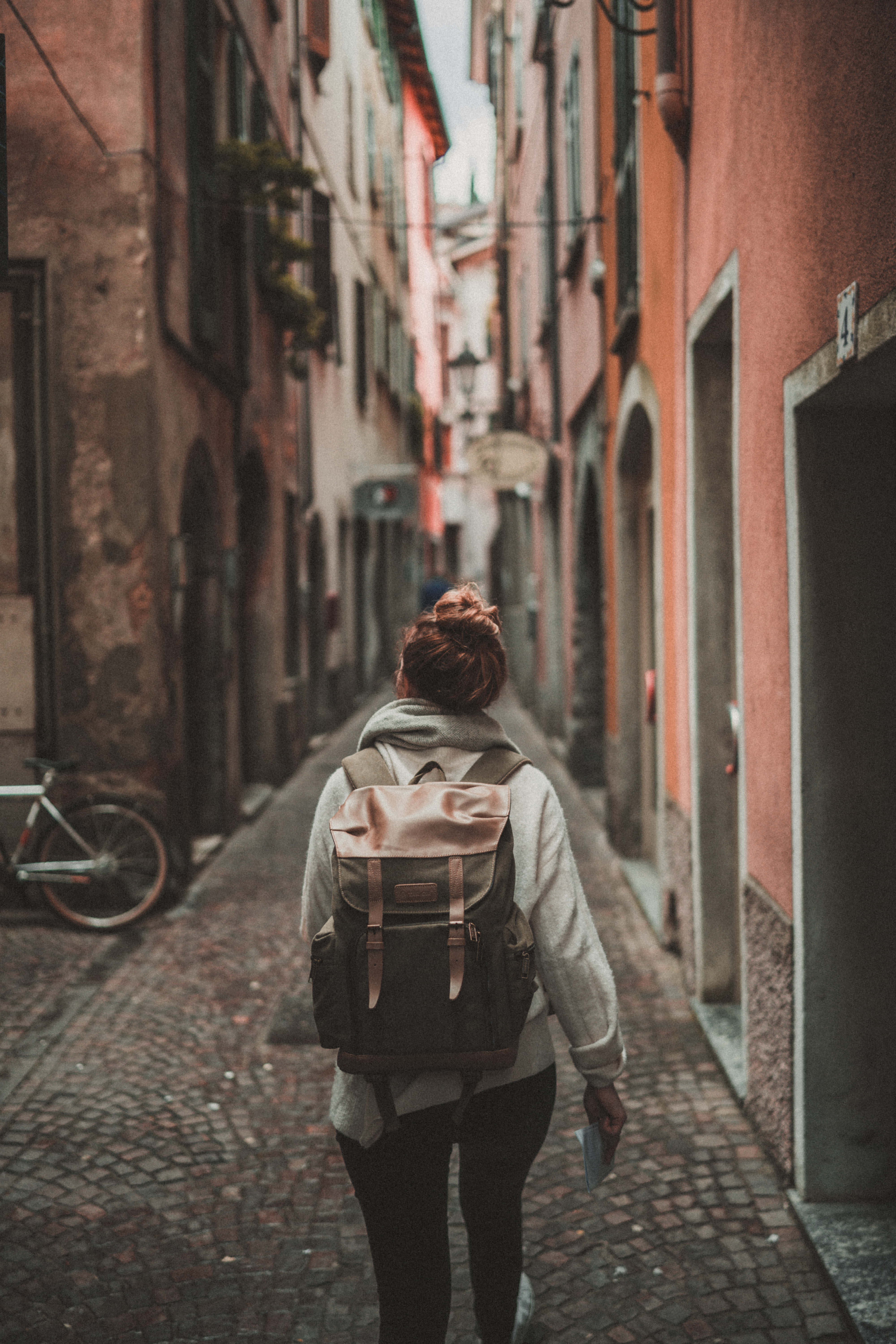 World Travel 桌布 壁紙 — 一個揹著背包的人沿著一條狹窄的鵝卵石小巷走遠，兩旁是色彩繽紛的歐洲建築。