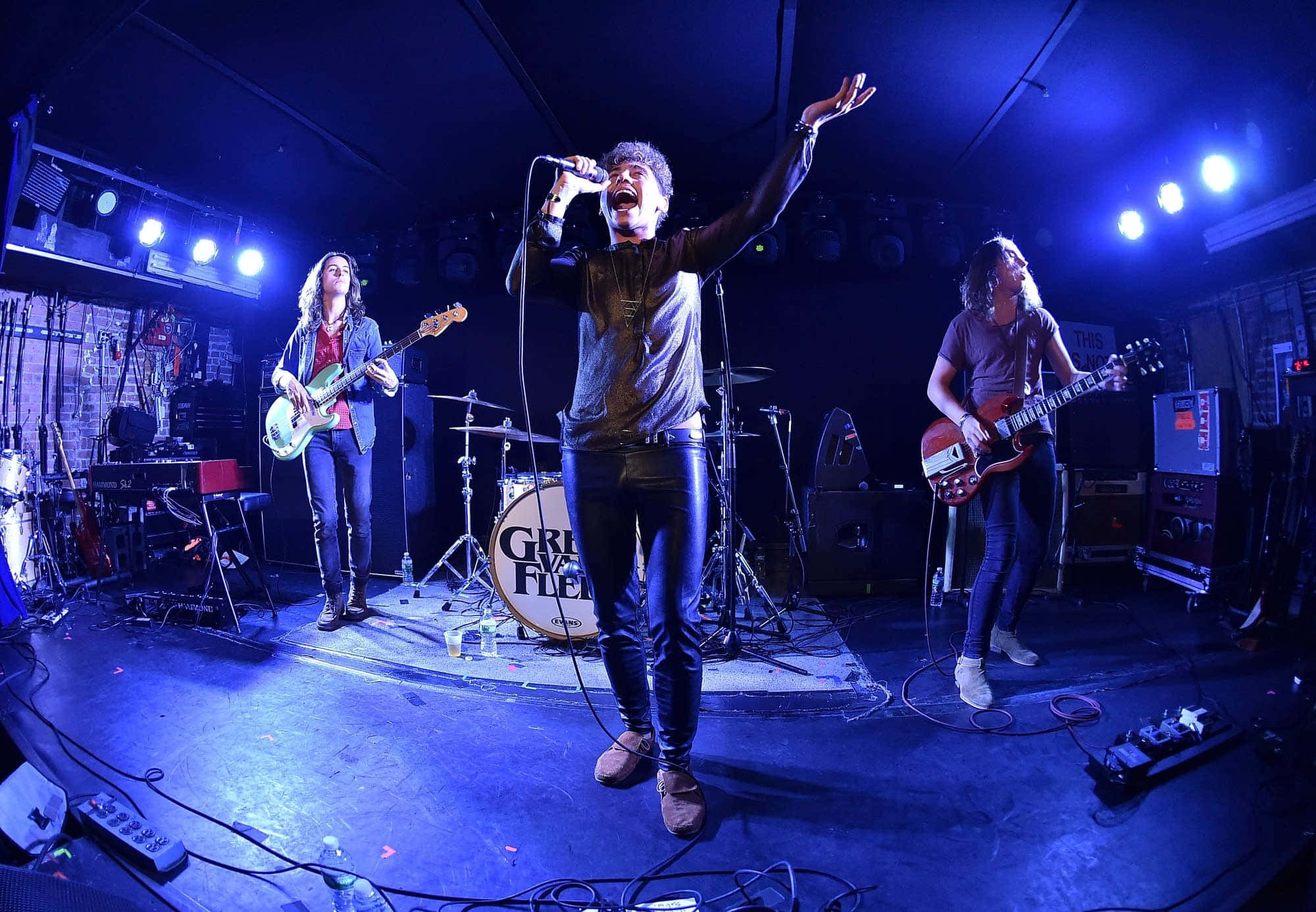 band 桌布 壁紙 — 一個搖滾樂團在昏暗的舞台上，沐浴在藍色燈光中，紙屑飄落，充滿活力地表演。