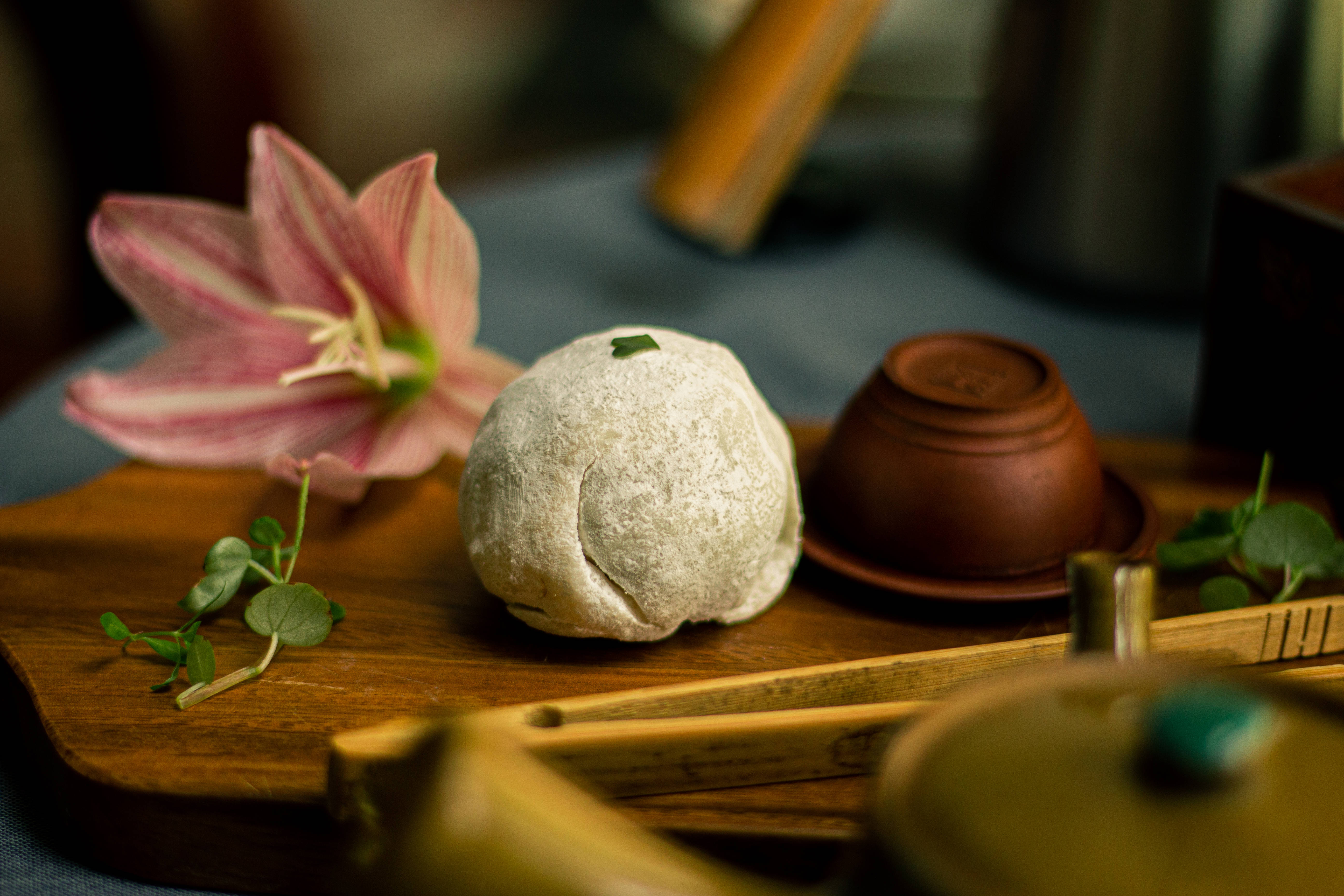 Mochi 桌布 壁紙 — 一個撒上糖粉的麻糬放在木托盤上，旁邊有一朵粉紅條紋花和茶具。