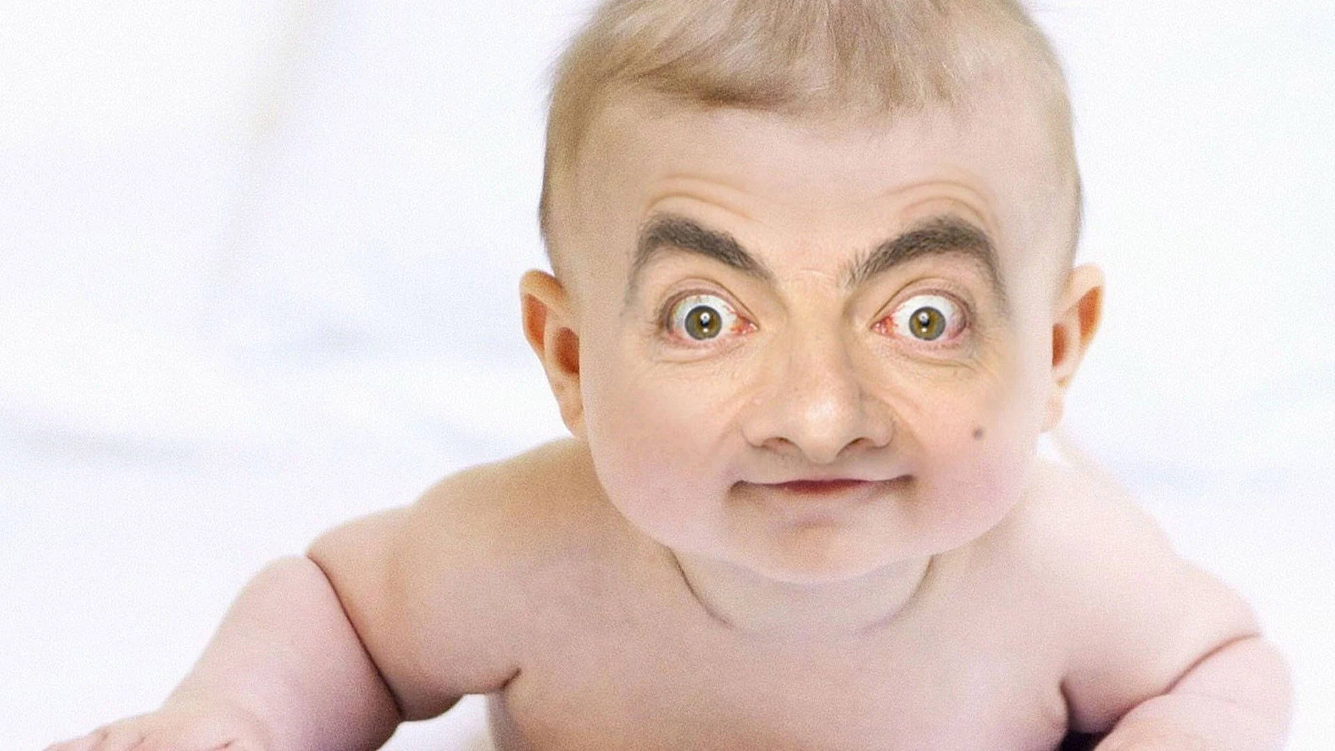 Funny Baby 桌布 壁紙 — 一個擁有Mr. Bean標誌性面孔的嬰兒，在柔和的白色背景下睜大眼睛咧嘴笑。
