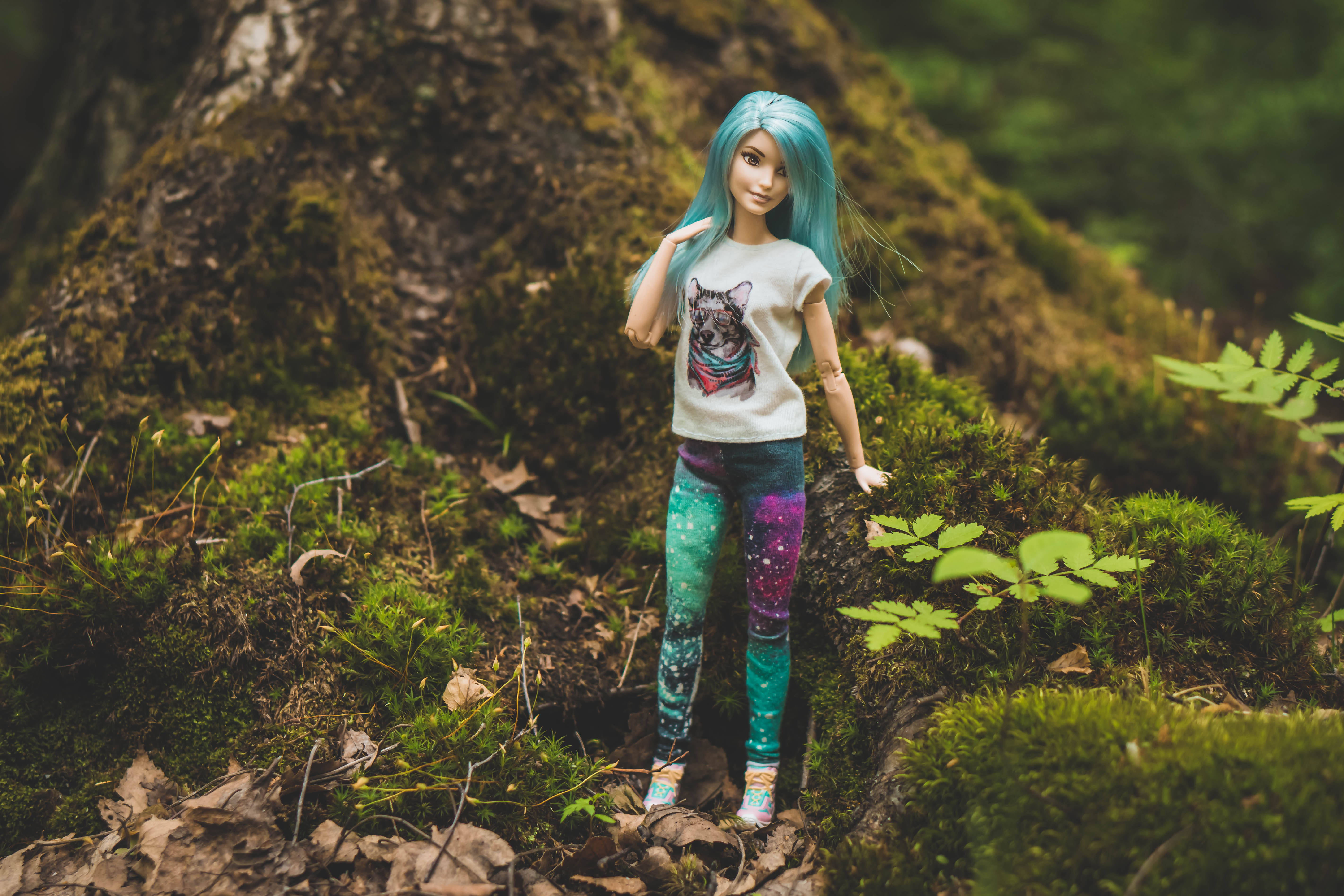 Doll 桌布 壁紙 — 一個擁有充滿活力的藍色頭髮和銀河緊身褲的娃娃，站在長滿苔蘚的森林地面和蕨類植物中。