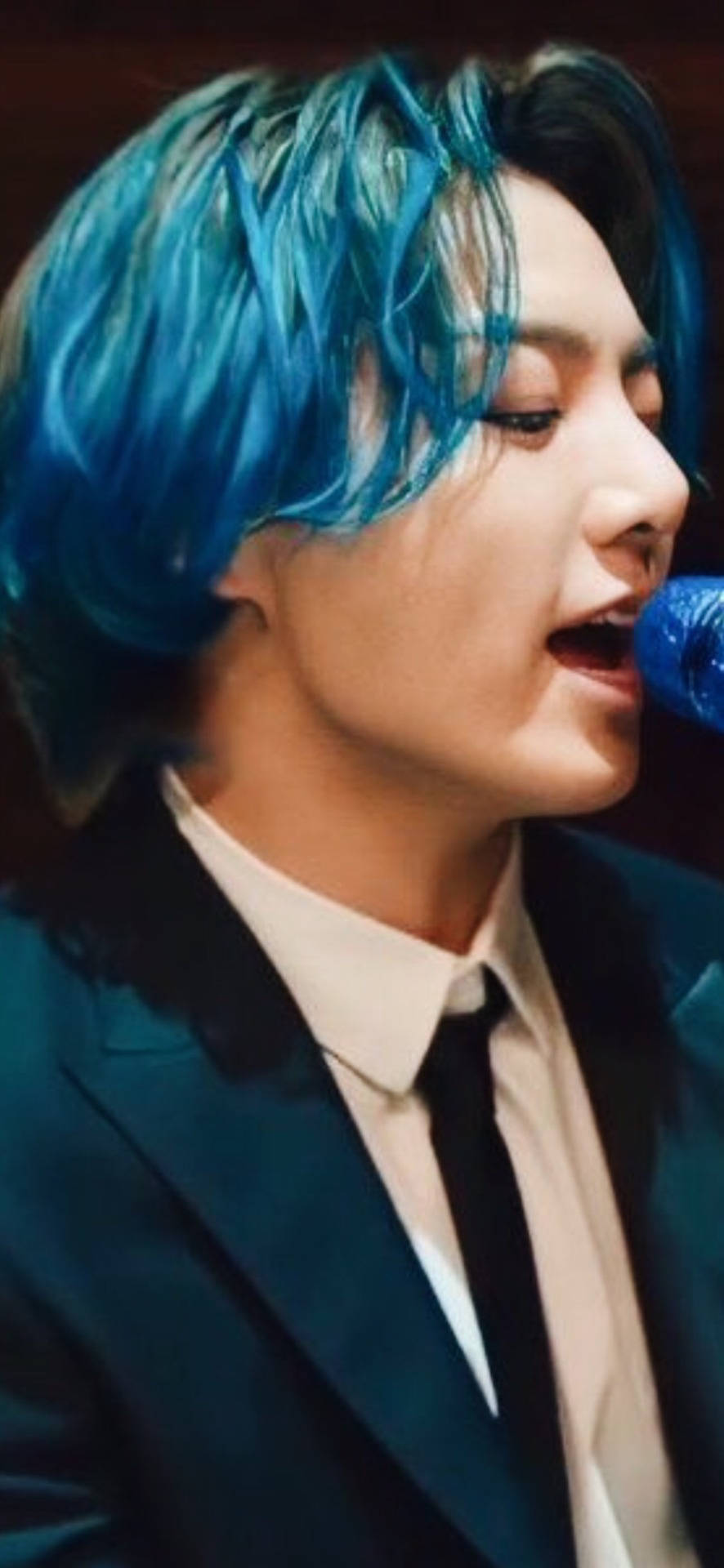 Singing 桌布 壁紙 — 一個擁有充滿活力的藍色頭髮的人，穿著深色西裝和白色襯衫，熱情地對著麥克風唱歌。