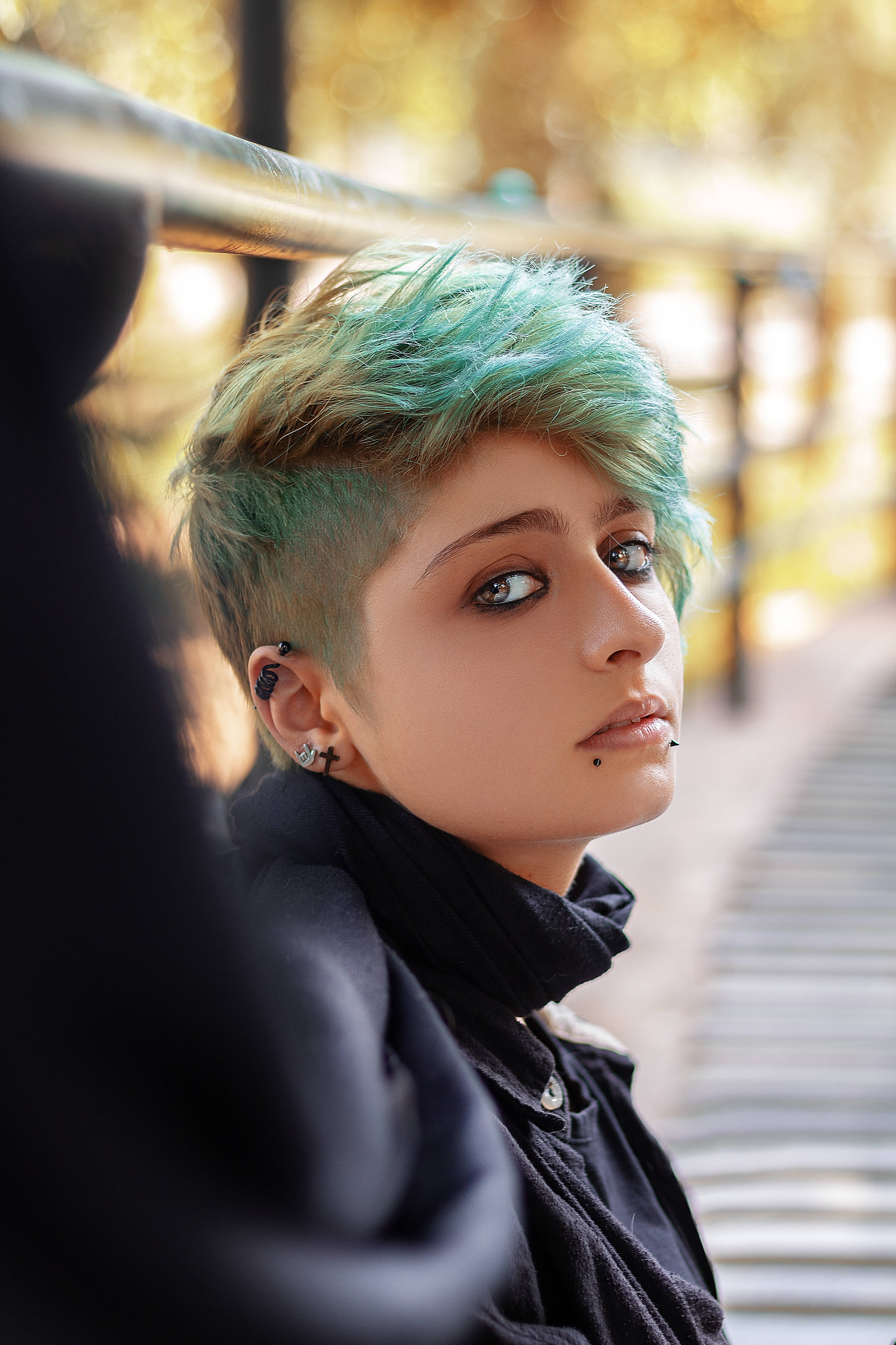 Tomboy 桌布 壁紙 — 一個擁有充滿活力的青綠色和金色短髮的人，在溫暖的金色陽光下若有所思地凝視著戶外。