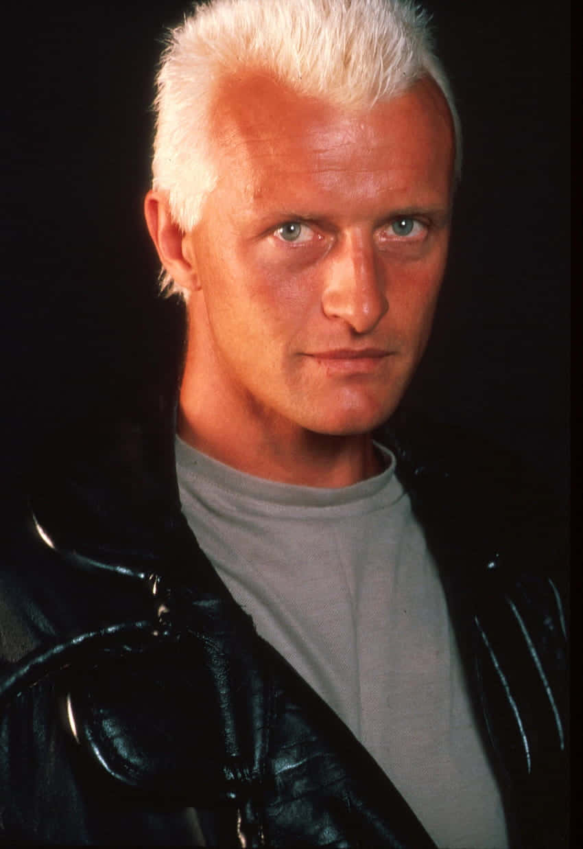 actor 桌布 壁紙 — 一個擁有尖刺白髮和銳利藍眼的男人，穿著黑色皮夾克，在黑暗背景下凝視著。