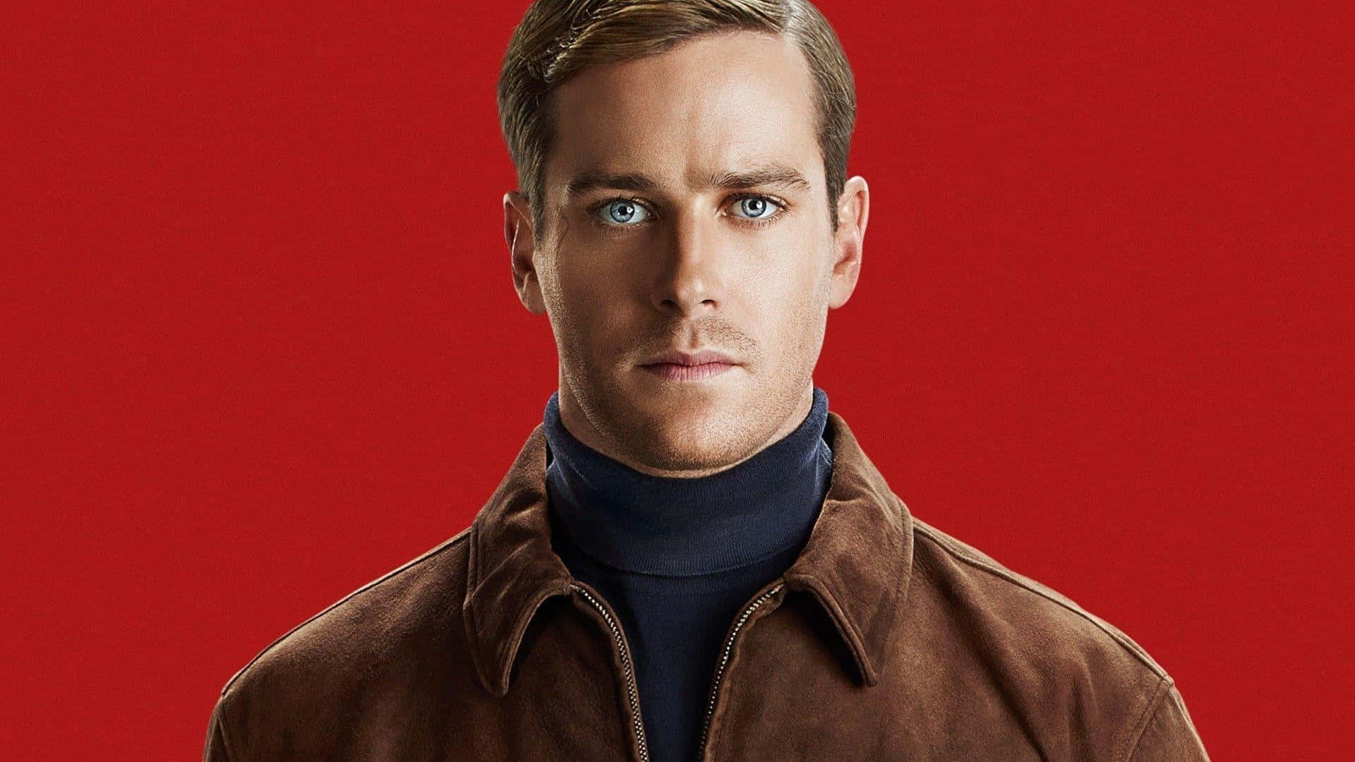 Armie Hammer 桌布 壁紙 — 一個擁有引人注目藍眼睛的男人，在鮮紅色背景下穿著棕色外套和深藍色高領毛衣，凝視著前方。