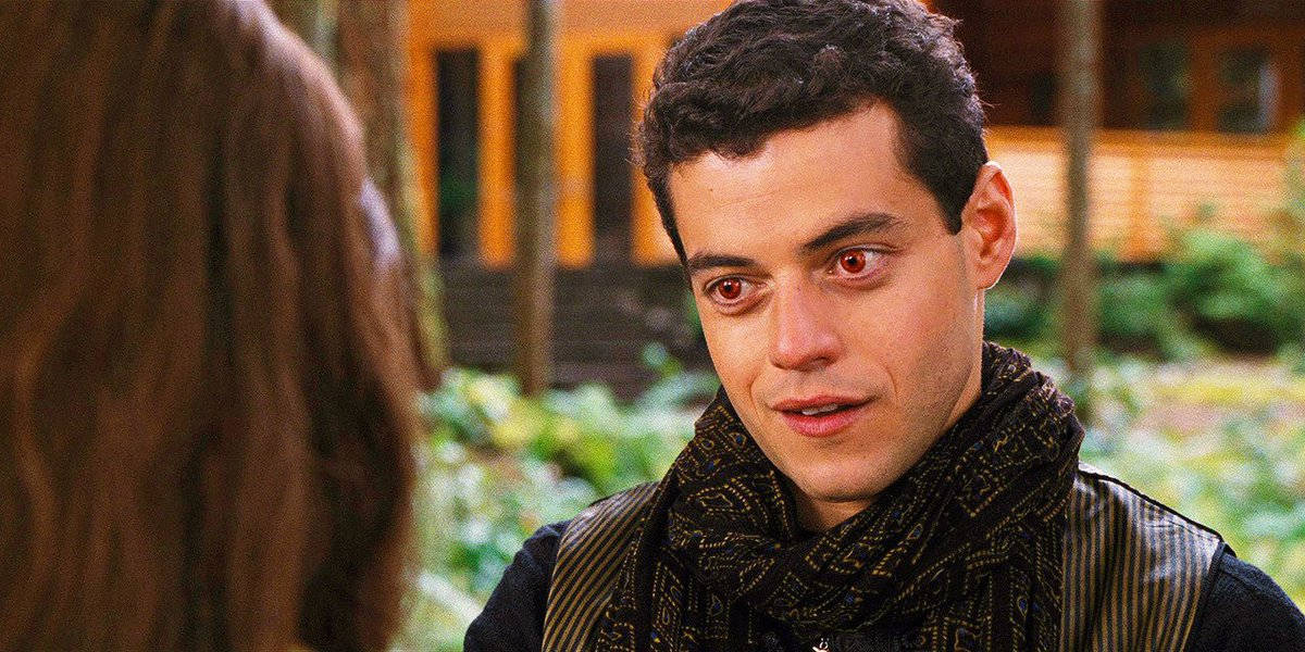Rami Malek 桌布 壁紙 — 一個擁有強烈紅眼和深色圍巾的男人，在木屋附近的森林區域凝視著一個女人。