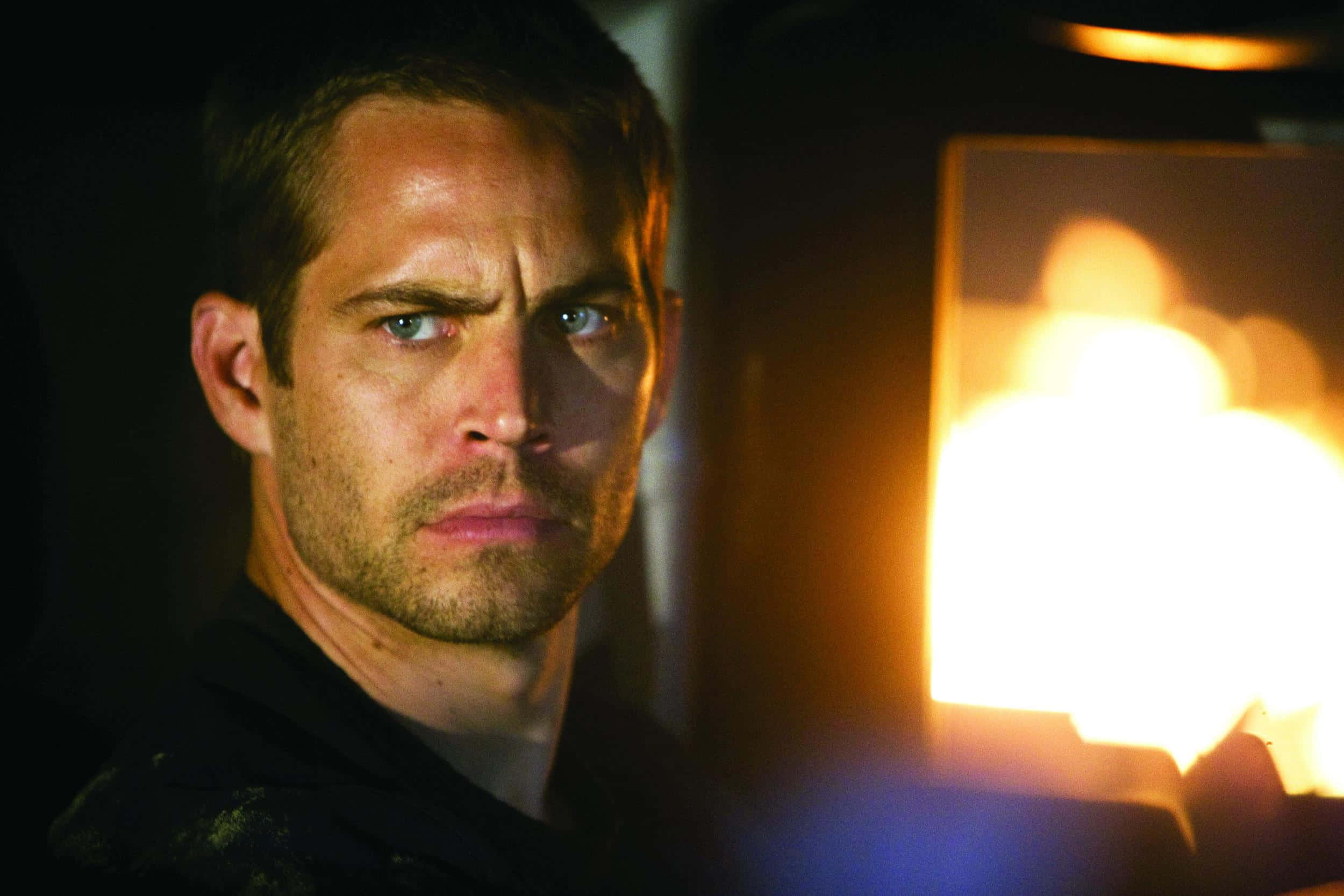 Paul Walker 桌布 壁紙 — 一個擁有強烈藍眼睛的男人在昏暗的車廂內向前凝視，身後有熾熱的橙色光芒。