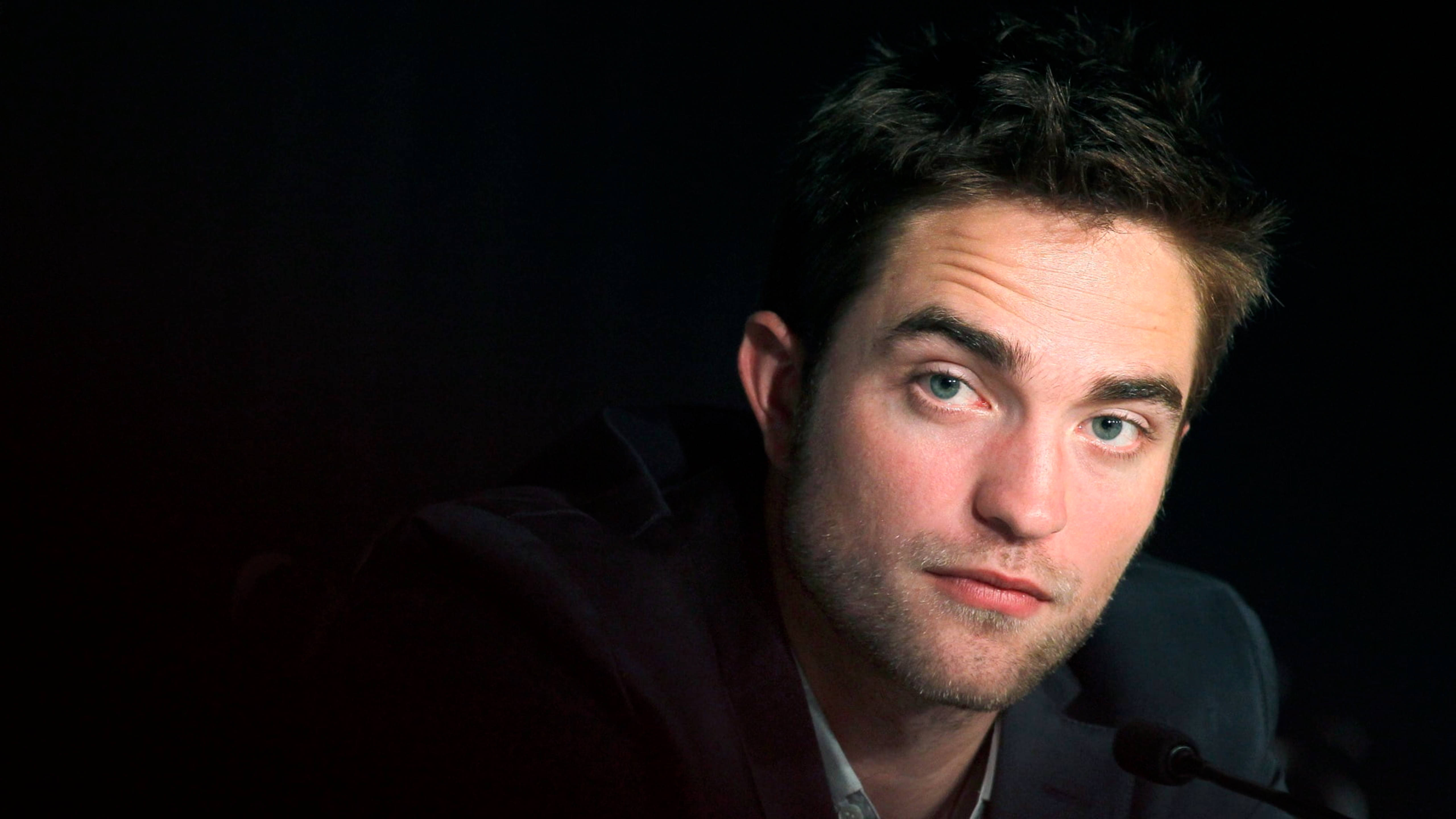 Robert Pattinson 桌布 壁紙 — 一個擁有強烈藍色眼睛和深色頭髮的男人在黑色背景前直視鏡頭。