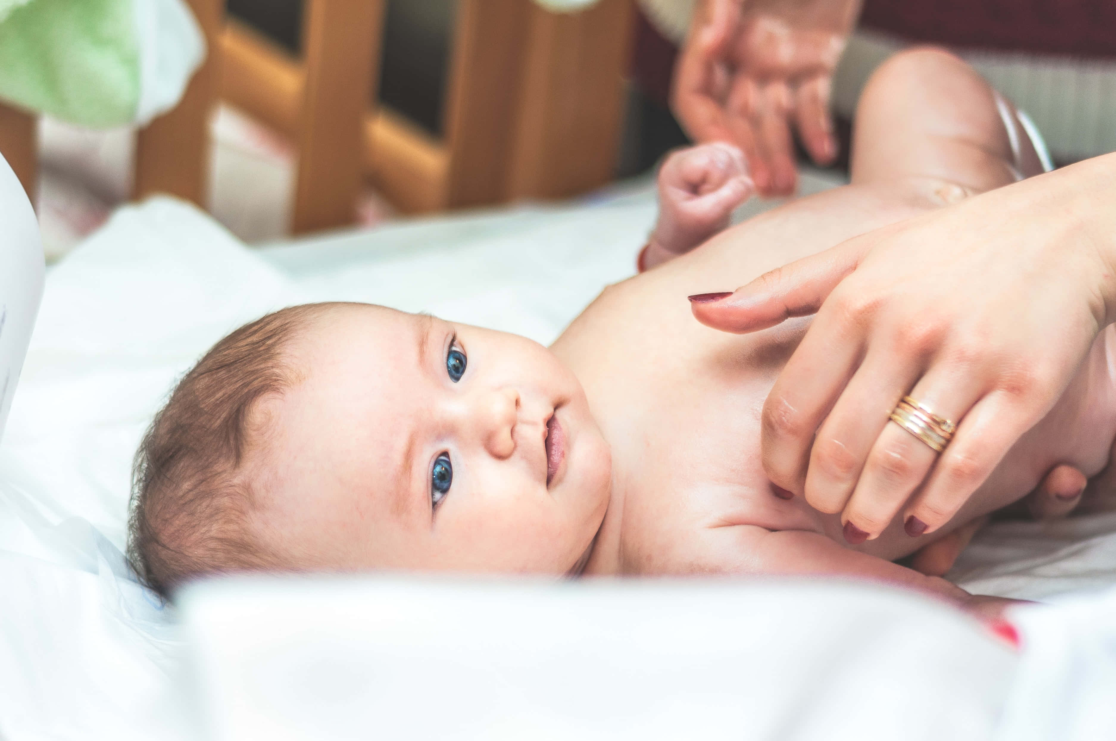 Baby Boy 桌布 壁紙 — 一個擁有明亮藍眼睛的新生嬰兒躺在白色床單上，成年人的手輕輕觸摸其胸部。