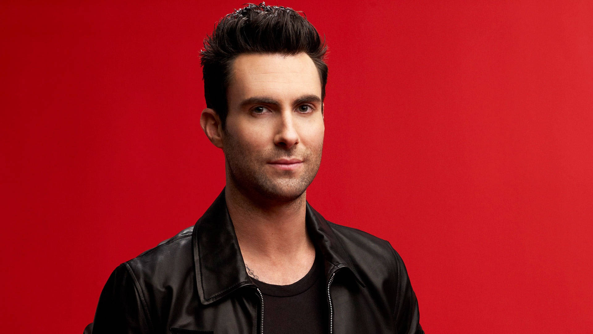 Adam Levine 桌布 壁紙 — 一個擁有時尚黑髮的男人穿著黑色皮夾克，背景為純紅色。