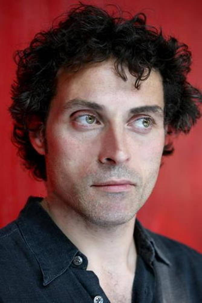 actor 桌布 壁紙 — 一個擁有深色捲髮和綠色眼睛的男人，在鮮紅色背景下向上凝視，穿著深色襯衫。