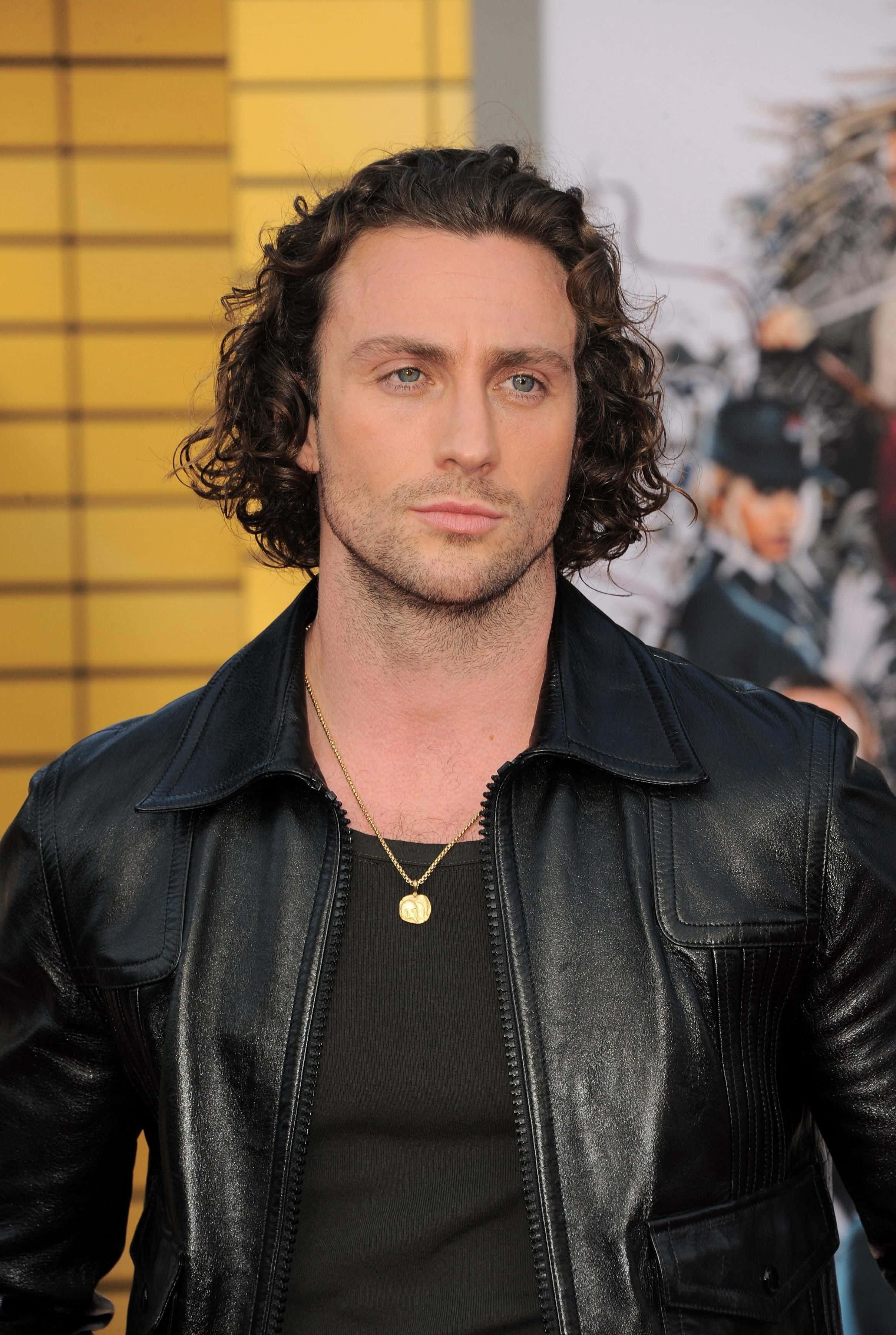 Celebrity 桌布 壁紙 — 一個擁有深色捲髮和藍眼睛的男人，穿著黑色皮夾克和金色項鍊，背景是黃色瓷磚牆。