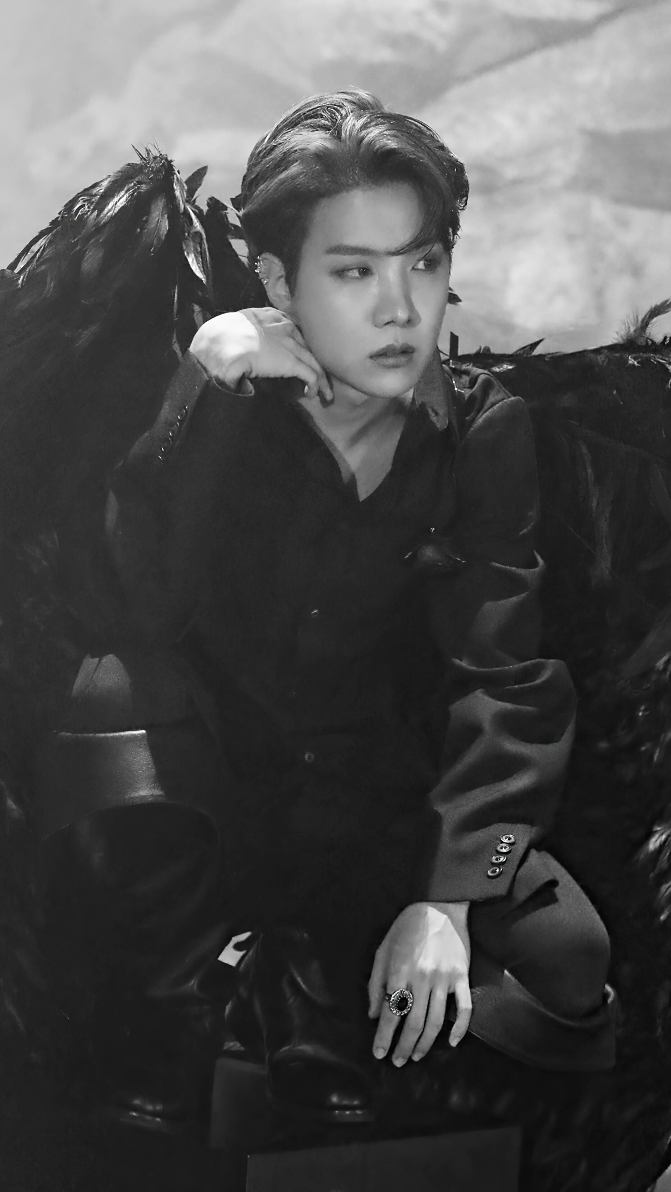 jhope 桌布 壁紙 — 一個擁有深色羽毛翅膀的人坐在戲劇性的黑白肖像中，手托下巴，穿著深色西裝和戒指。