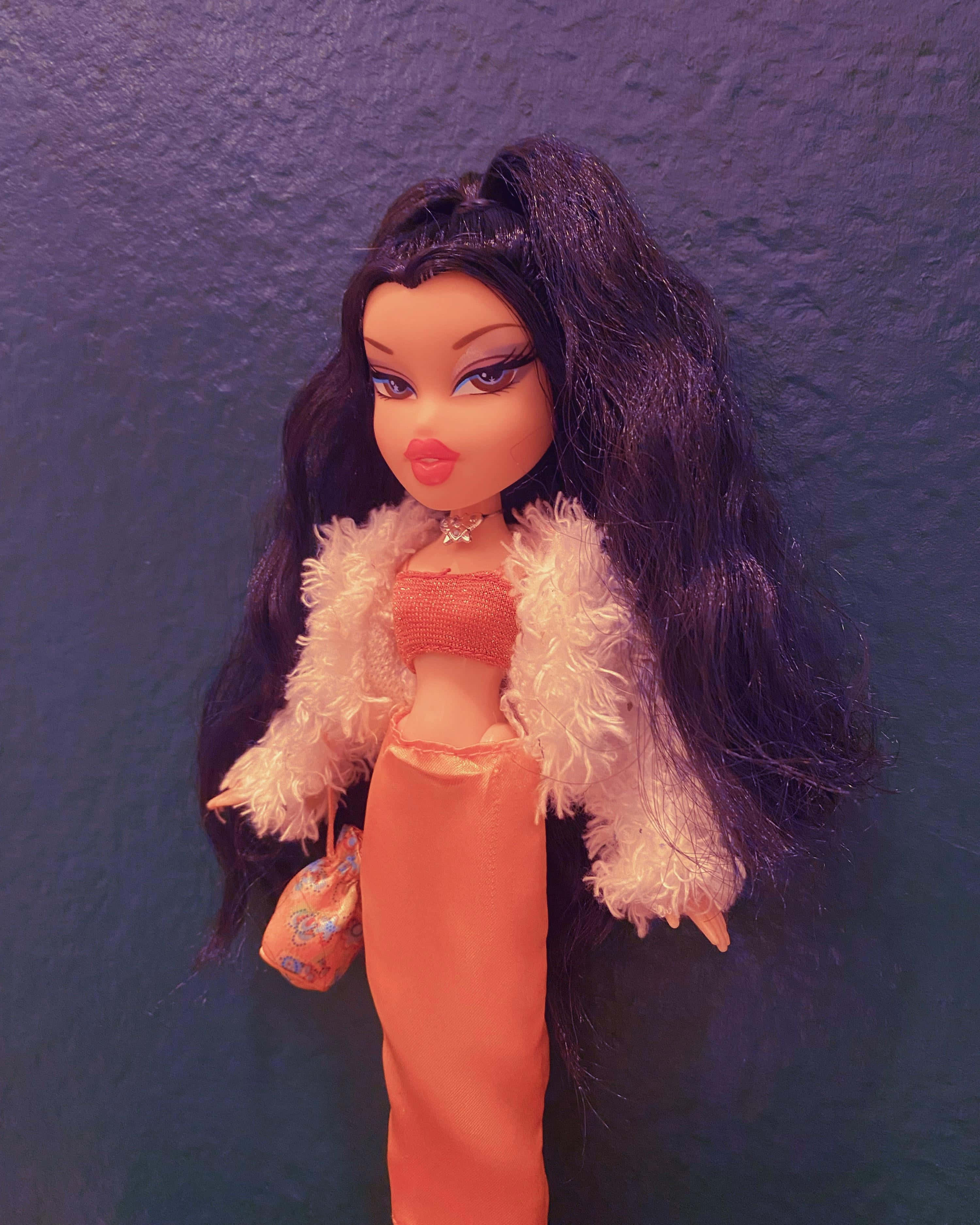 bratz 美學 桌布 壁紙 — 一個擁有深色長髮和鮮豔妝容的 Bratz 公仔，穿著帶有毛茸茸白色領子的桃色服裝，背景是質感紫色牆壁。