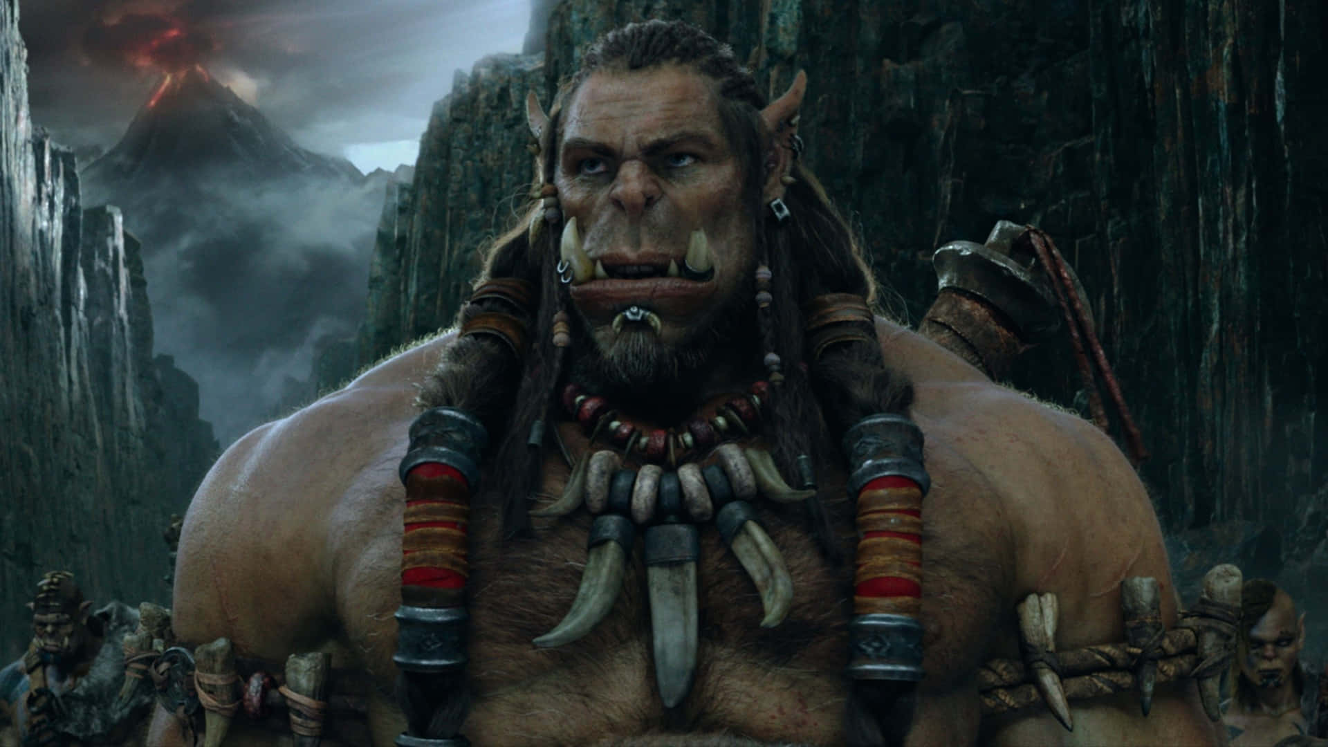Warcraft 2 桌布 壁紙 — 一個擁有獠牙和部落裝備的兇猛獸人 warlord 站在黑暗奇幻背景的火山山脈前。