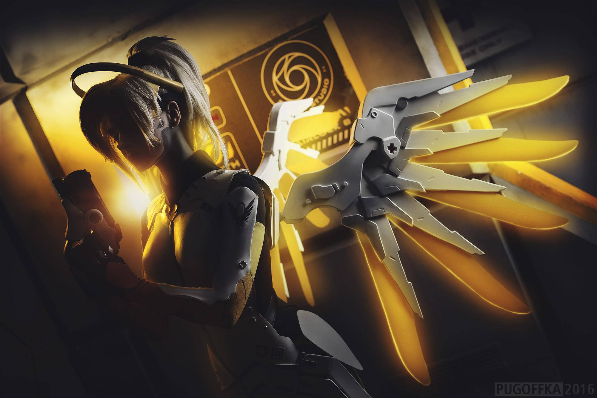 Mercy 桌布 壁紙 — 一個擁有發光金色翅膀和機械手臂的網路天使，站在燈光昏暗的未來主義走廊中。