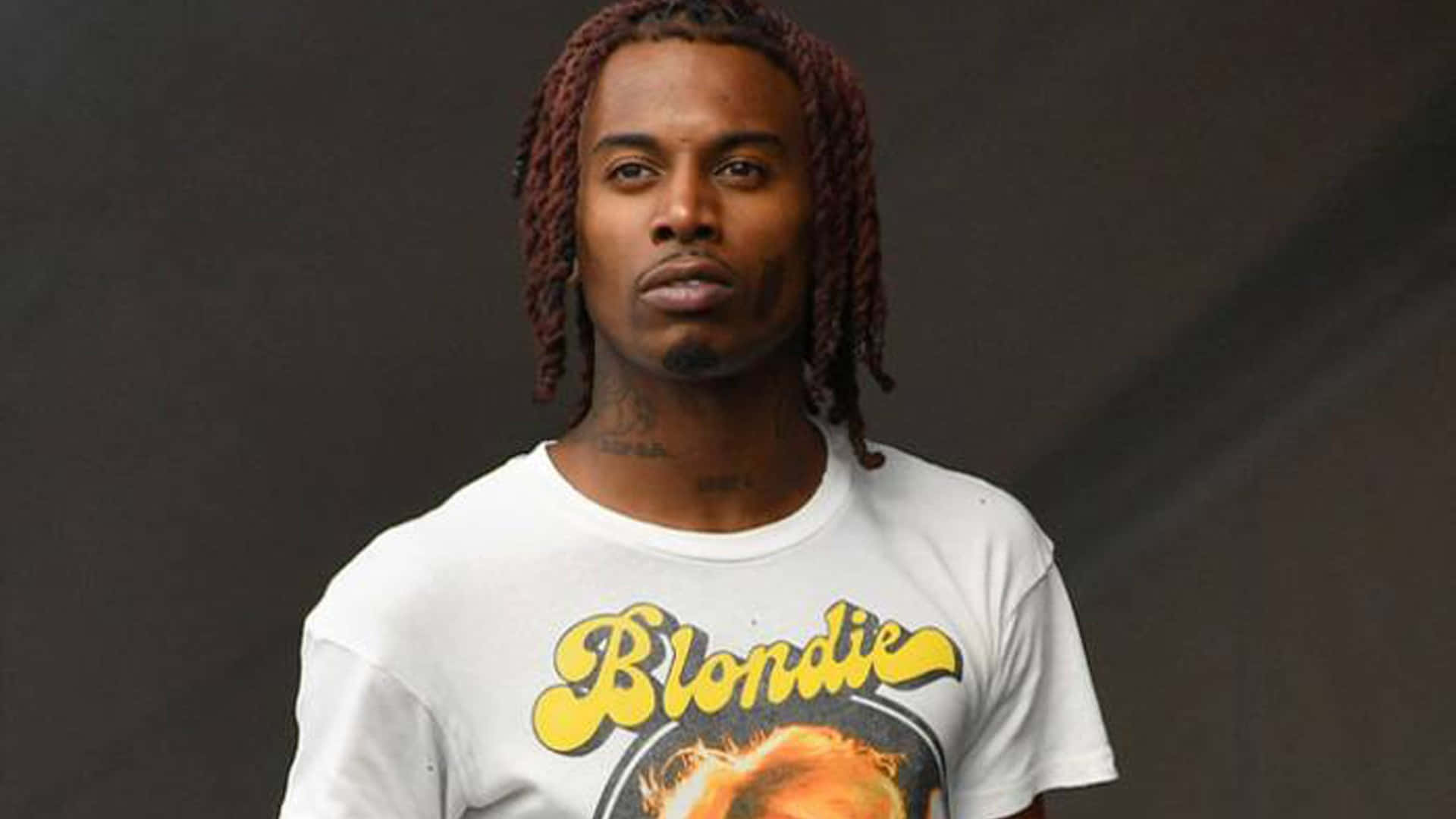 Playboi Carti HD 桌布 壁紙 — 一個擁有紅褐色辮子頭的男人直視鏡頭，穿著一件印有Blondie樂隊圖案的白T恤。