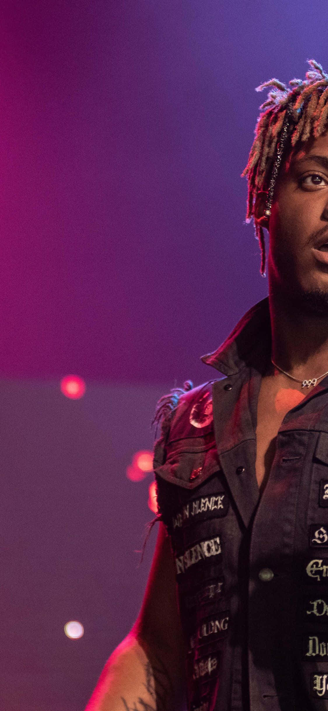 Rappers 桌布 壁紙 — 一個擁有色彩繽紛辮子頭和鉚釘背心的男人，站在充滿活力的紫色和紅色舞台燈光下。