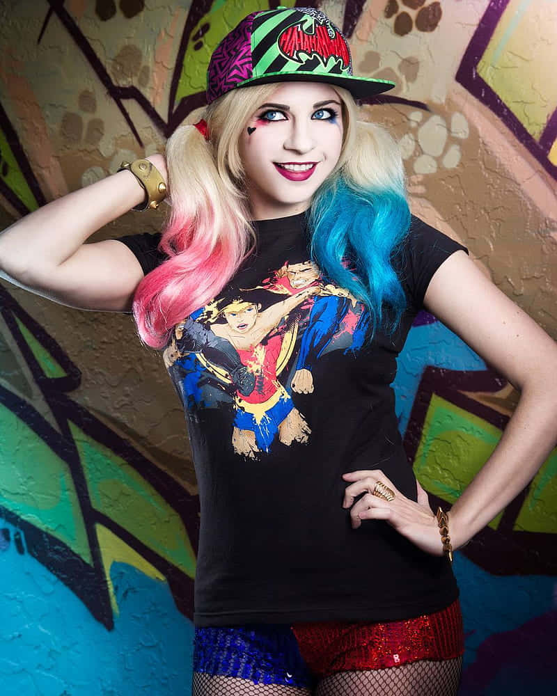 Harley Quinn Cosplay 桌布 壁紙 — 一個擁有色彩繽紛頭髮和大膽妝容的人，自信地在一幅充滿活力的塗鴉牆前擺姿勢，穿著漫畫T恤和亮片短褲。