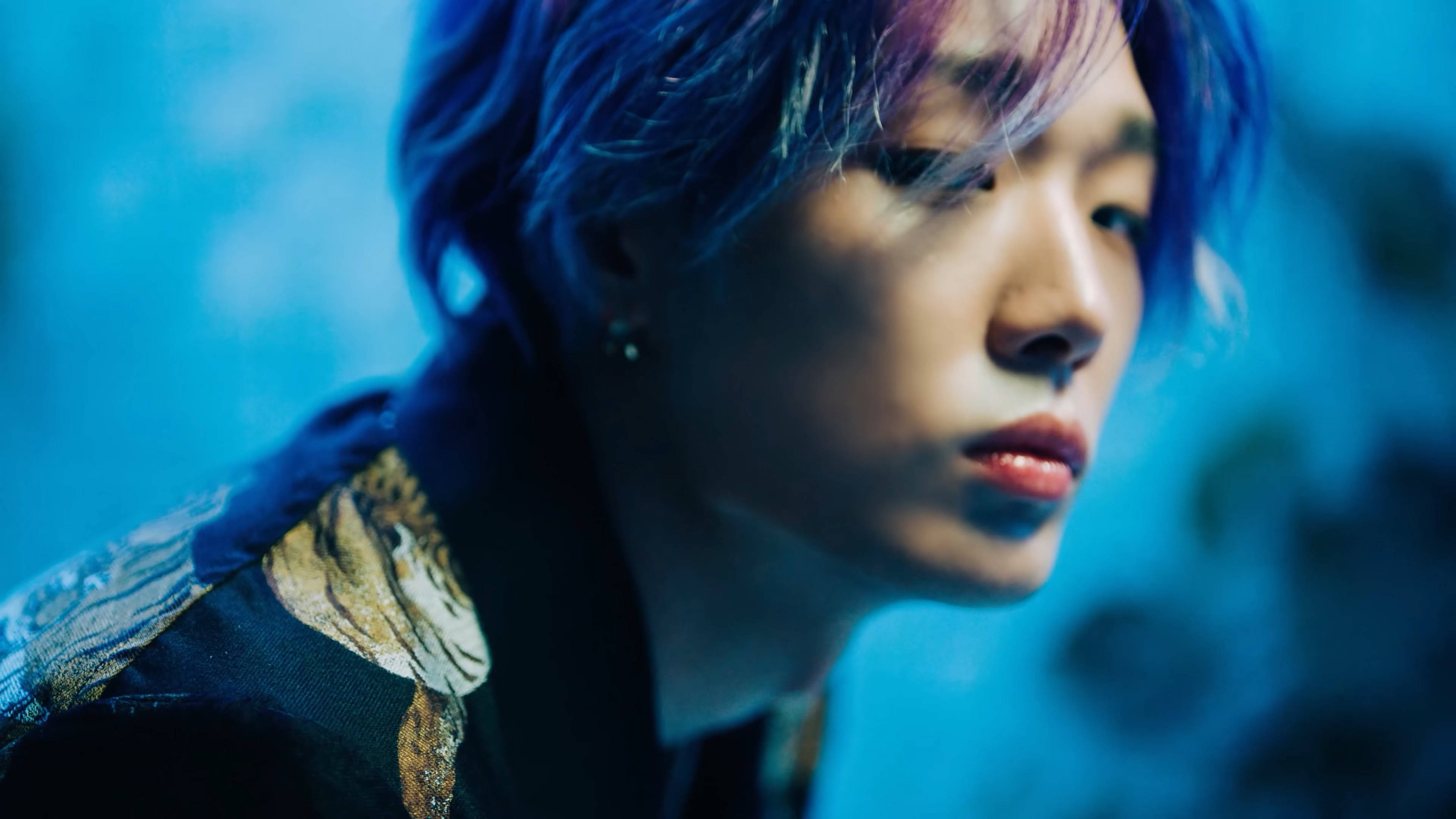 Ikon 桌布 壁紙 — 一個擁有藍色和紫色頭髮的人，在清涼的藍色模糊背景下若有所思地凝視著。