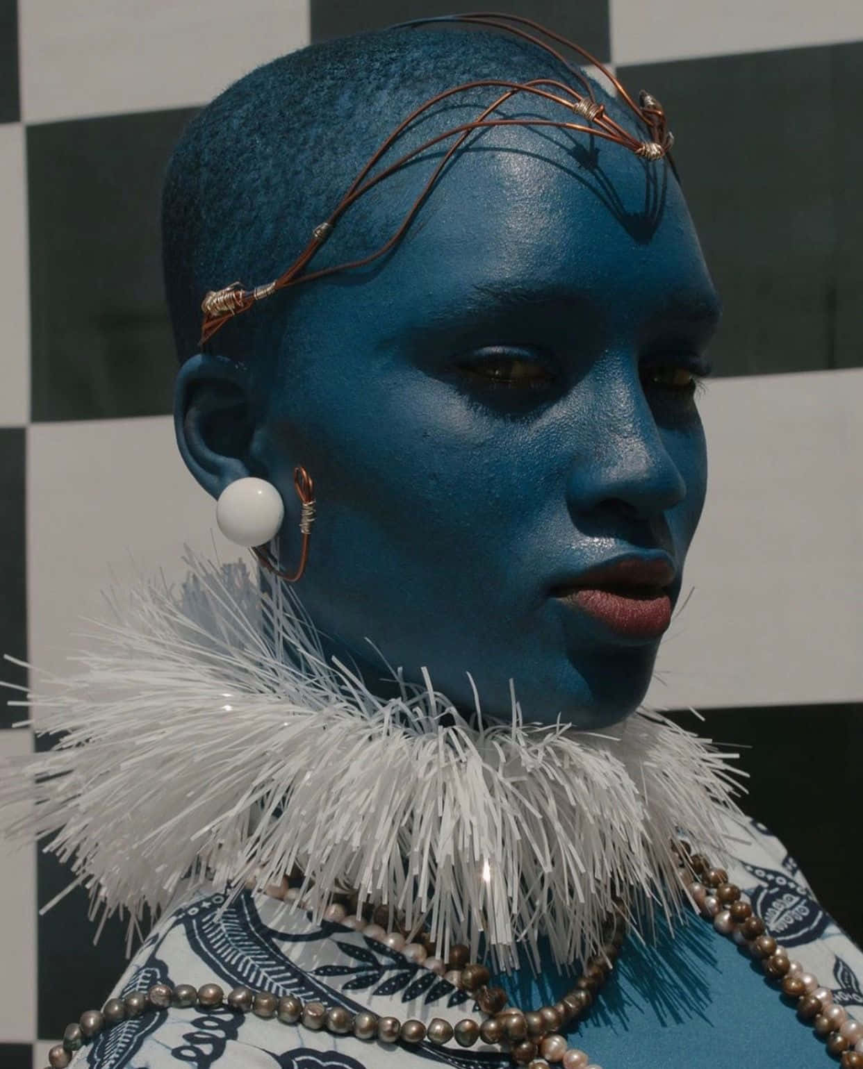 Afrofuturism 桌布 壁紙 — 一個擁有藍色皮膚和銅線頭飾的人，在黑白格子背景前擺姿勢。