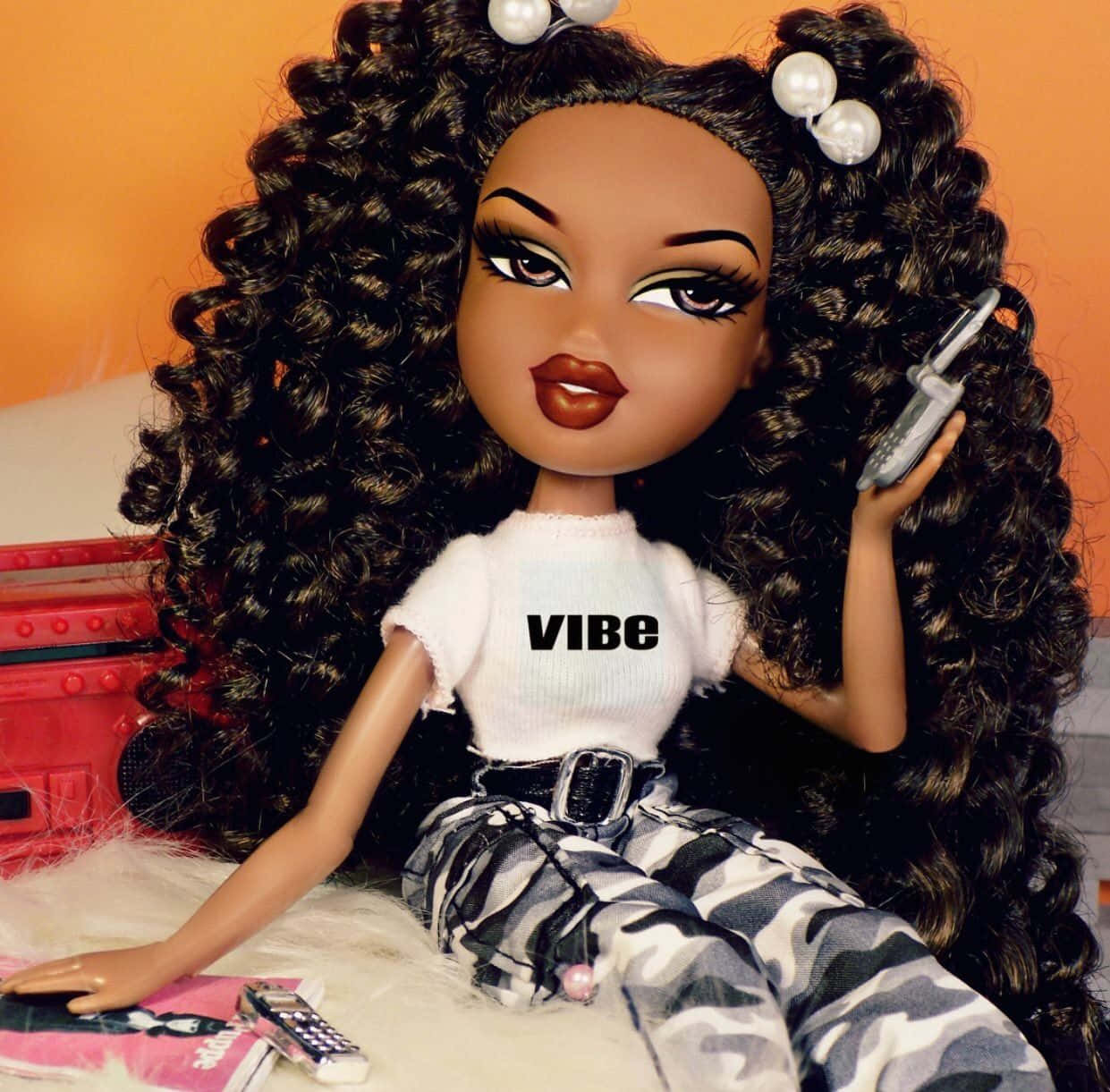 桌布 壁紙 — 一個擁有豐盈捲髮和珍珠夾的 Bratz 娃娃，正躺在毛絨絨的地毯上，拿著一支摺疊手機。
