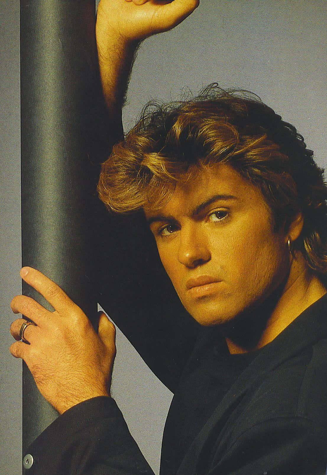 George Michael 桌布 壁紙 — 一個擁有豐盈金髮的男人在戲劇性燈光的攝影棚中靠著柱子。