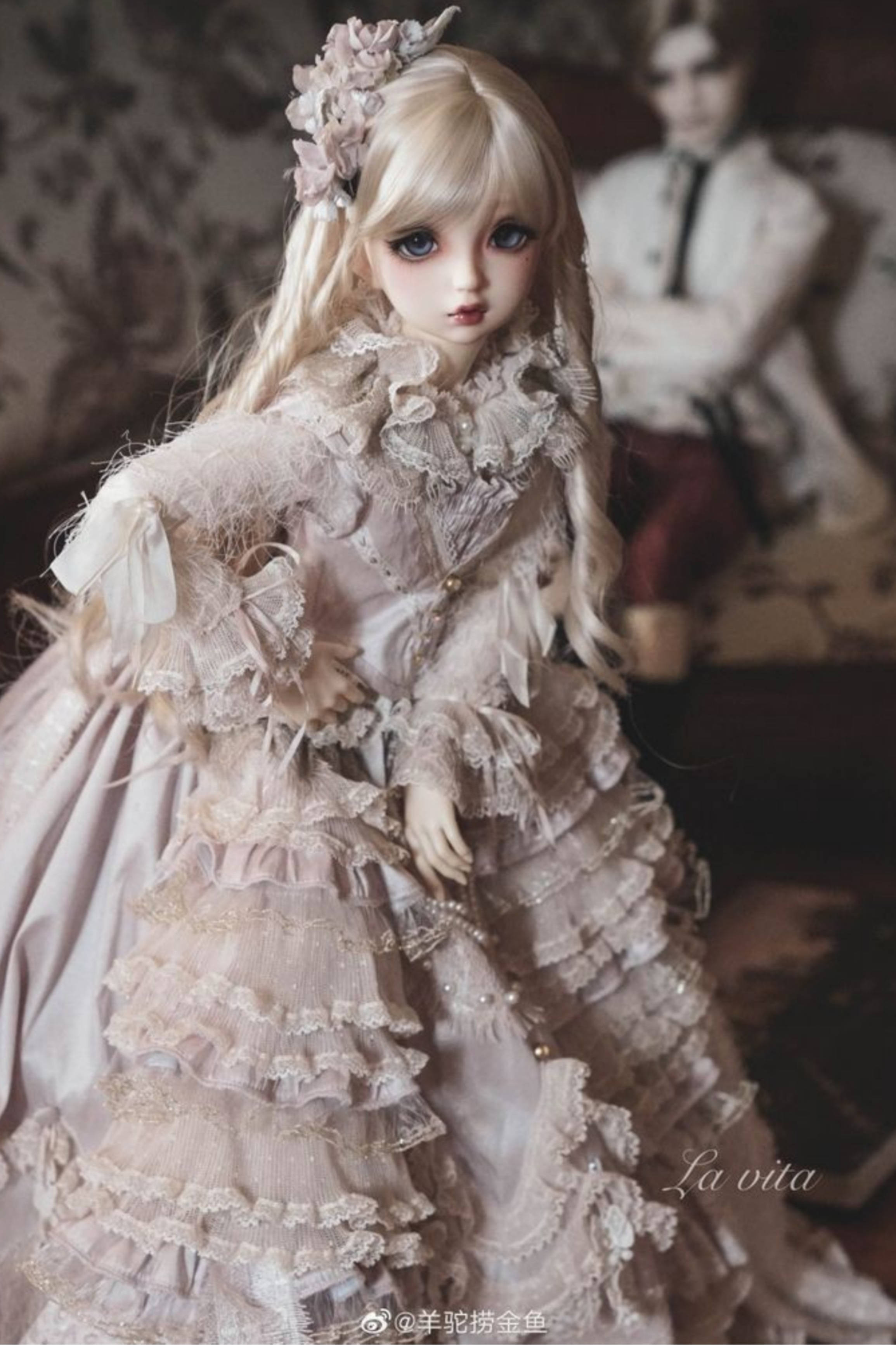 Doll 桌布 壁紙 — 一個擁有金色長髮和花卉頭飾的洋娃娃，在柔和光線的復古房間裡，穿著一件精緻的淡粉紅色蕾絲長裙，飾有荷葉邊和珍珠。