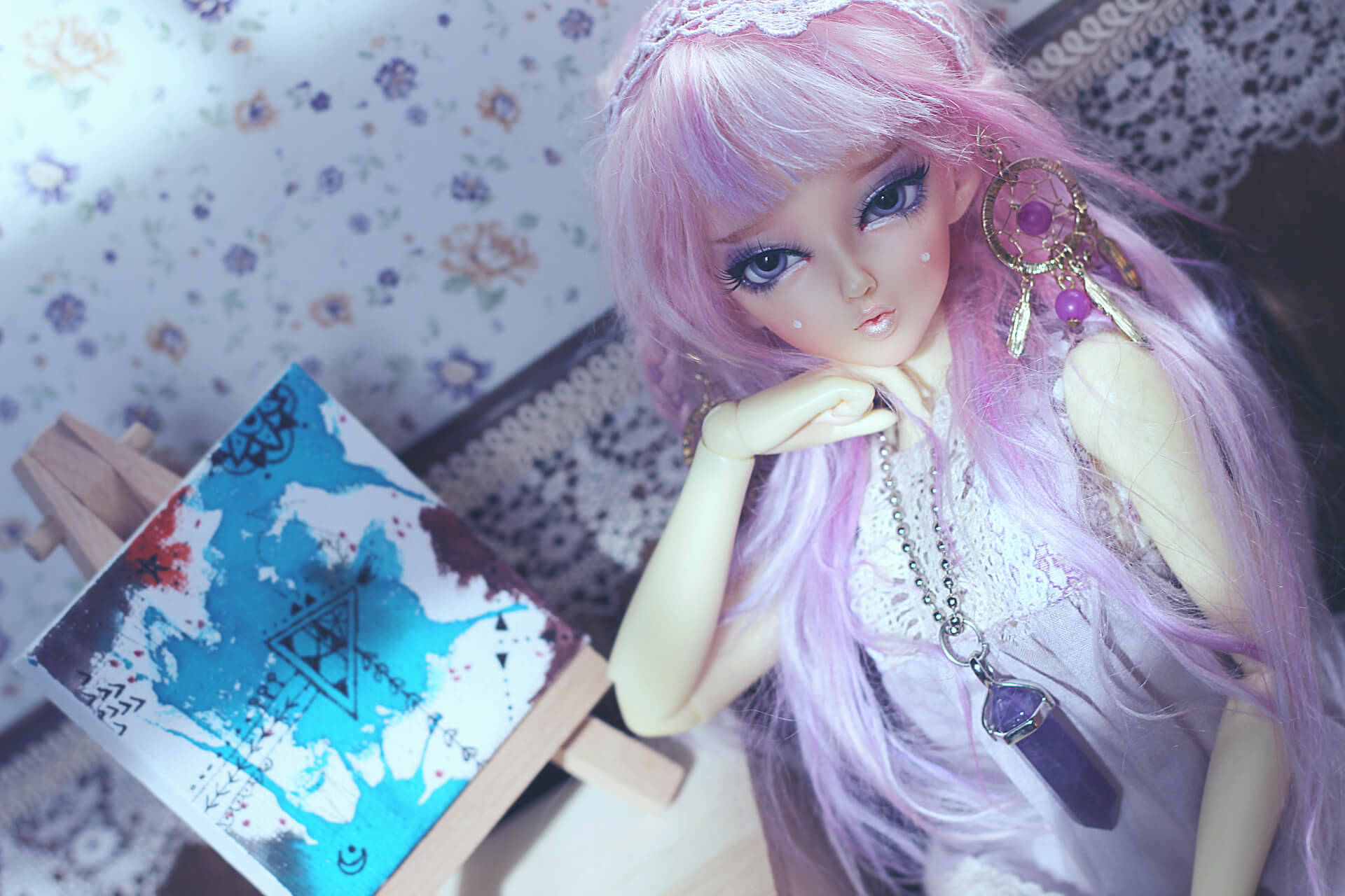 Doll 桌布 壁紙 — 一個擁有長長粉紅色頭髮和捕夢網耳環的洋娃娃，坐在畫架上的抽象畫旁邊，背景是花卉壁紙。