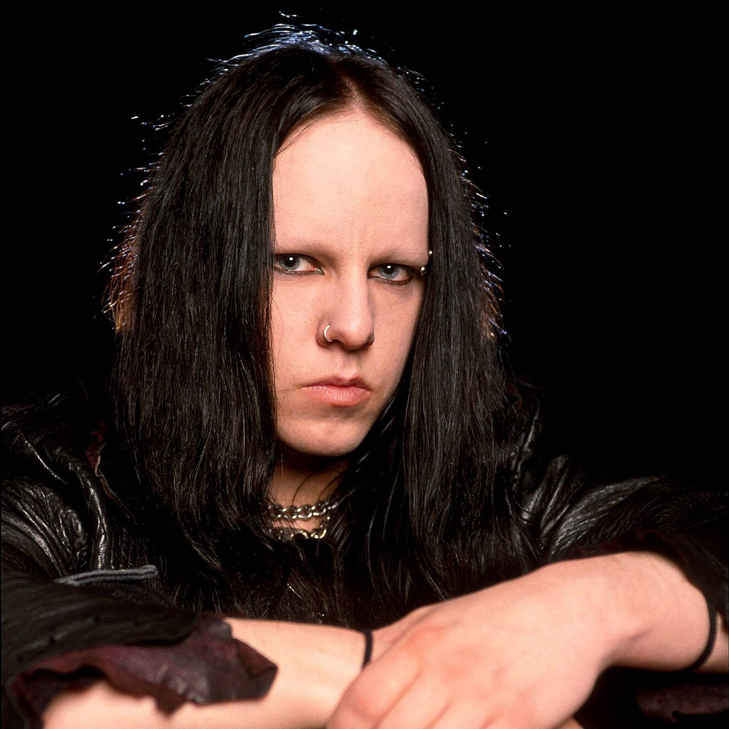 Joey Jordison 桌布 壁紙 — 一個擁有長長黑髮和銳利藍眼睛的人，在黑色背景前穿著皮夾克，凝視著。