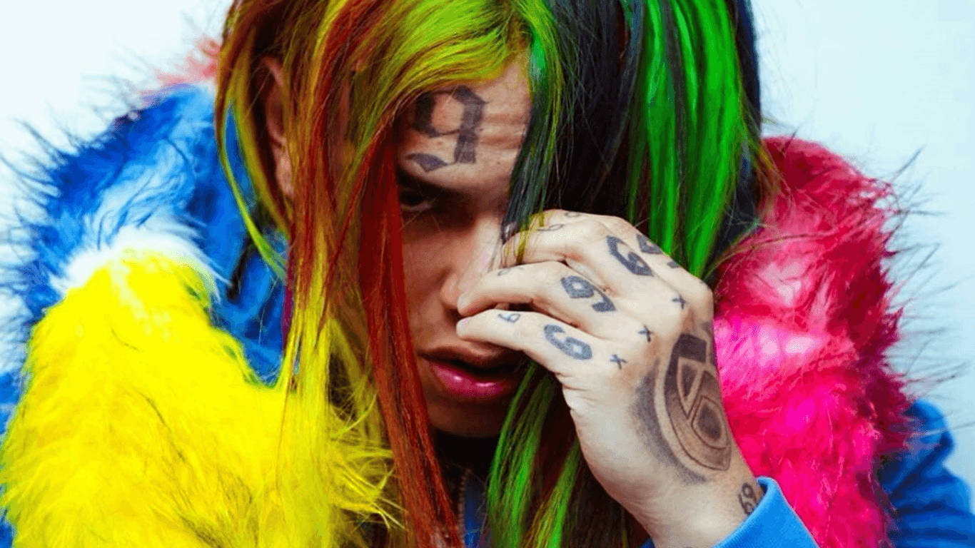 Tattoo 桌布 壁紙 — 一個擁有鮮豔彩虹頭髮和刺青的人，穿著色彩繽紛的絨毛外套，用手遮住臉。