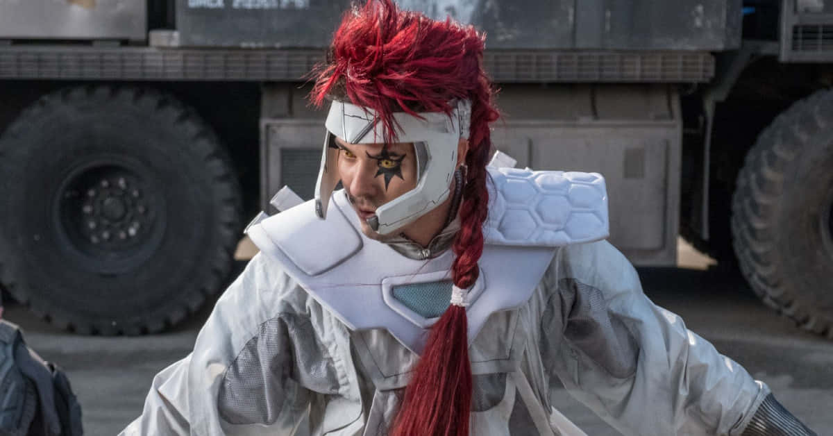 Shatterstar 桌布 壁紙 — 一個擁有鮮豔紅髮和未來感白色盔甲的人站在一輛軍用卡車前，背景是粗糙的戶外環境。