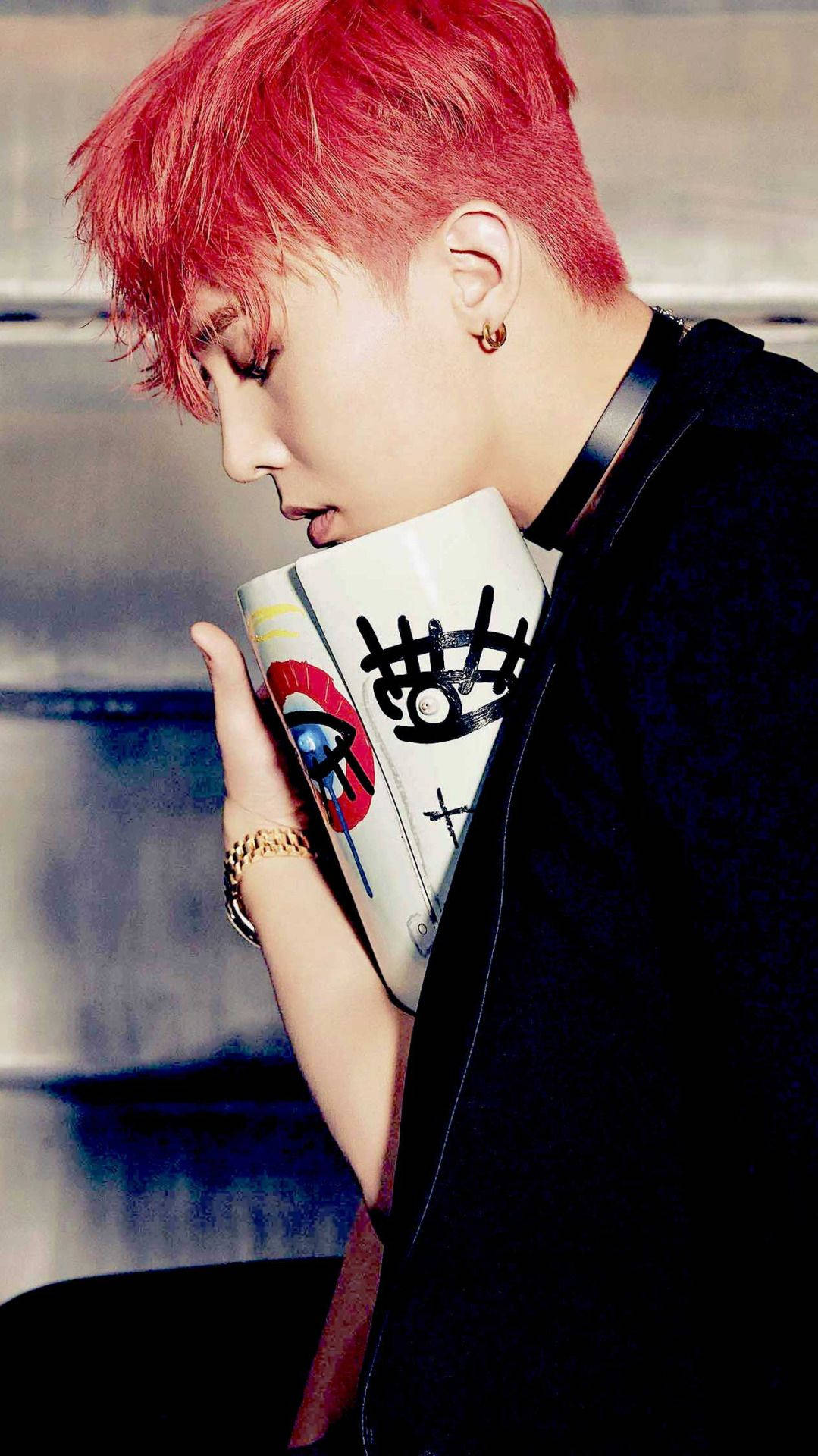 G-dragon 桌布 壁紙 — 一個擁有鮮豔紅髮的人，在模糊的城市背景下，從一個帶有醒目普普風眼睛的馬克杯啜飲。